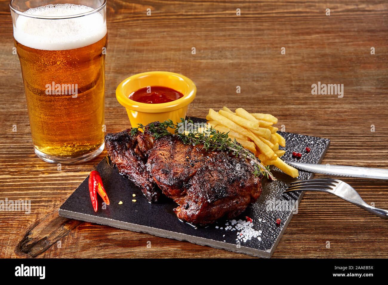 Vaso de cerveza con filete gourmet y patatas fritas en el fondo de madera. Foto de stock