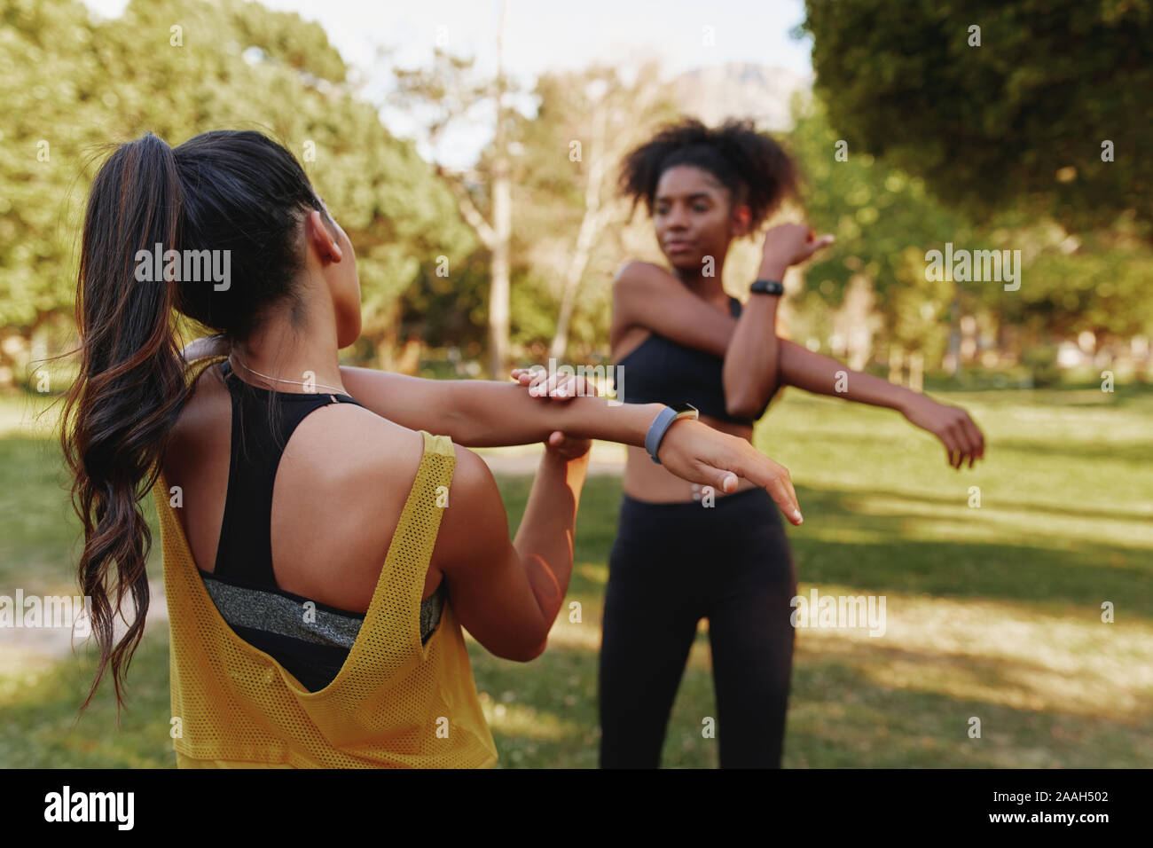 Dos jóvenes de gimnasia deportiva femenina diversos amigos de estirar sus músculos en el parque en un día de verano - dos amigos que trabajan juntos Foto de stock