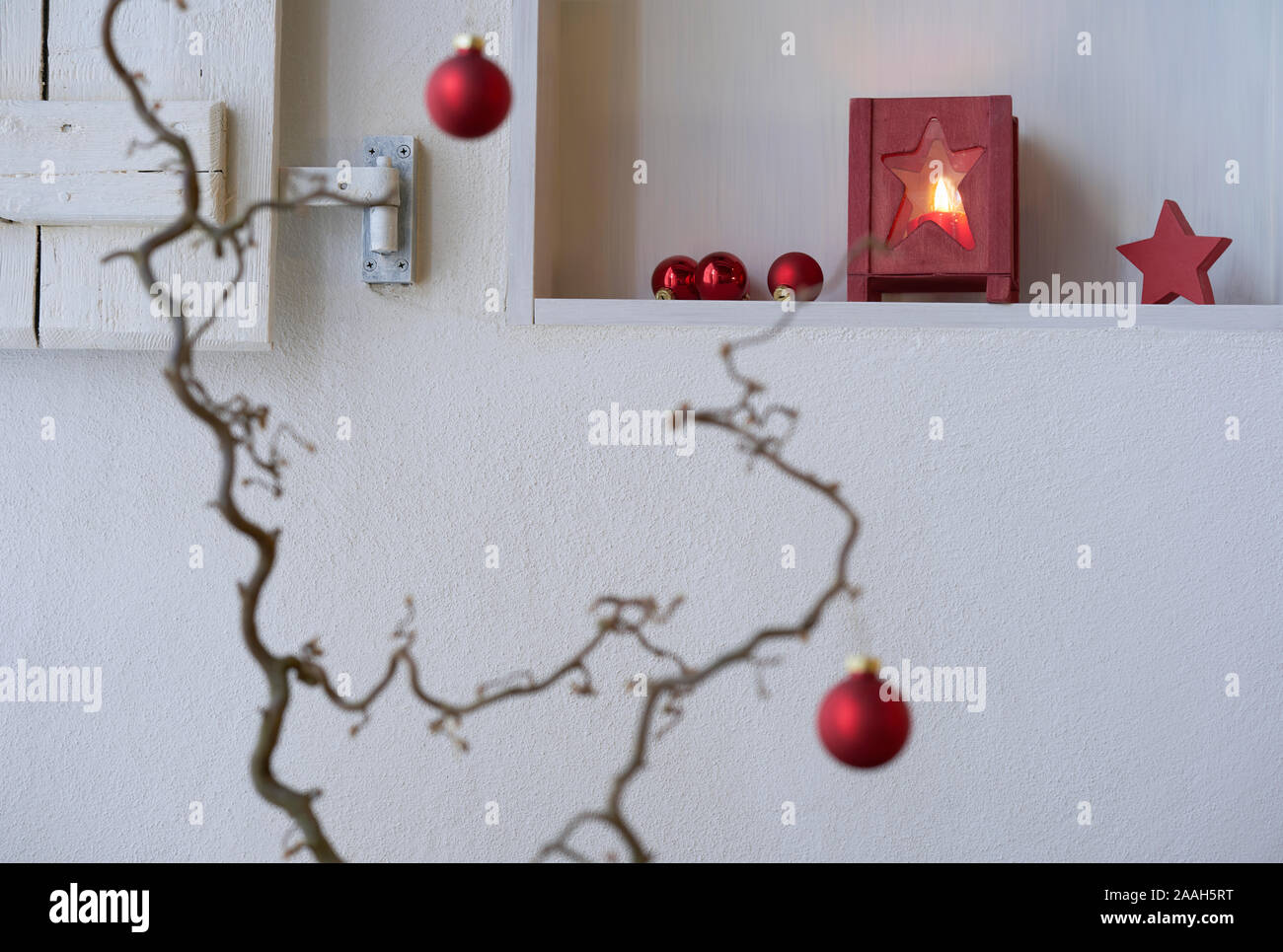 Unsharp rojo bolas de navidad en una rama delante de un estante con decoración de Navidad roja, linterna con luz de velas, estrella roja Foto de stock