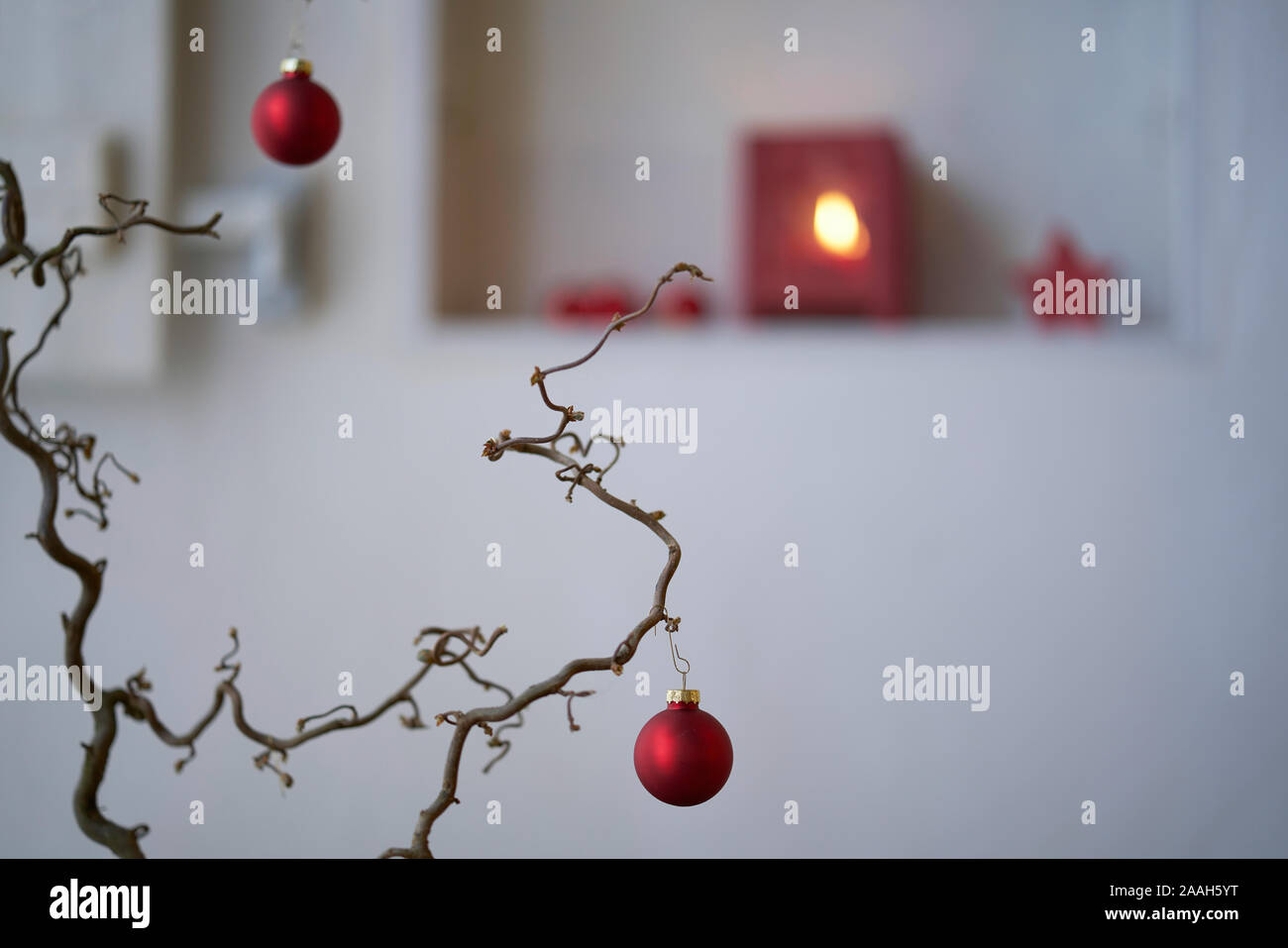 Bolas de Navidad de color rojo en una rama delante de un fondo de desenfoque con un estante con decoración de Navidad roja, linterna con luz de velas, estrella roja Foto de stock
