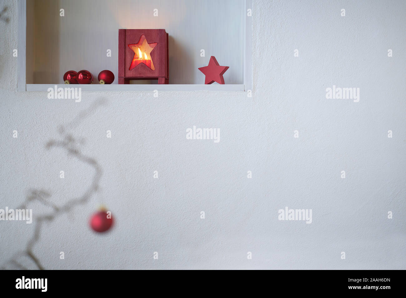 Unsharp rojo bolas de navidad en una rama delante de un estante con decoración de Navidad roja, linterna con luz de velas, estrella roja Foto de stock