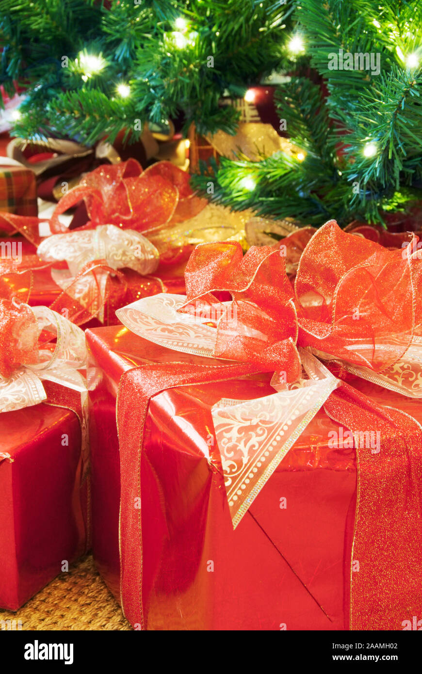 Grandes regalos envueltos en papel brillante rojo con arcos decorativos y cintas debajo de un árbol de Navidad. Foto de stock