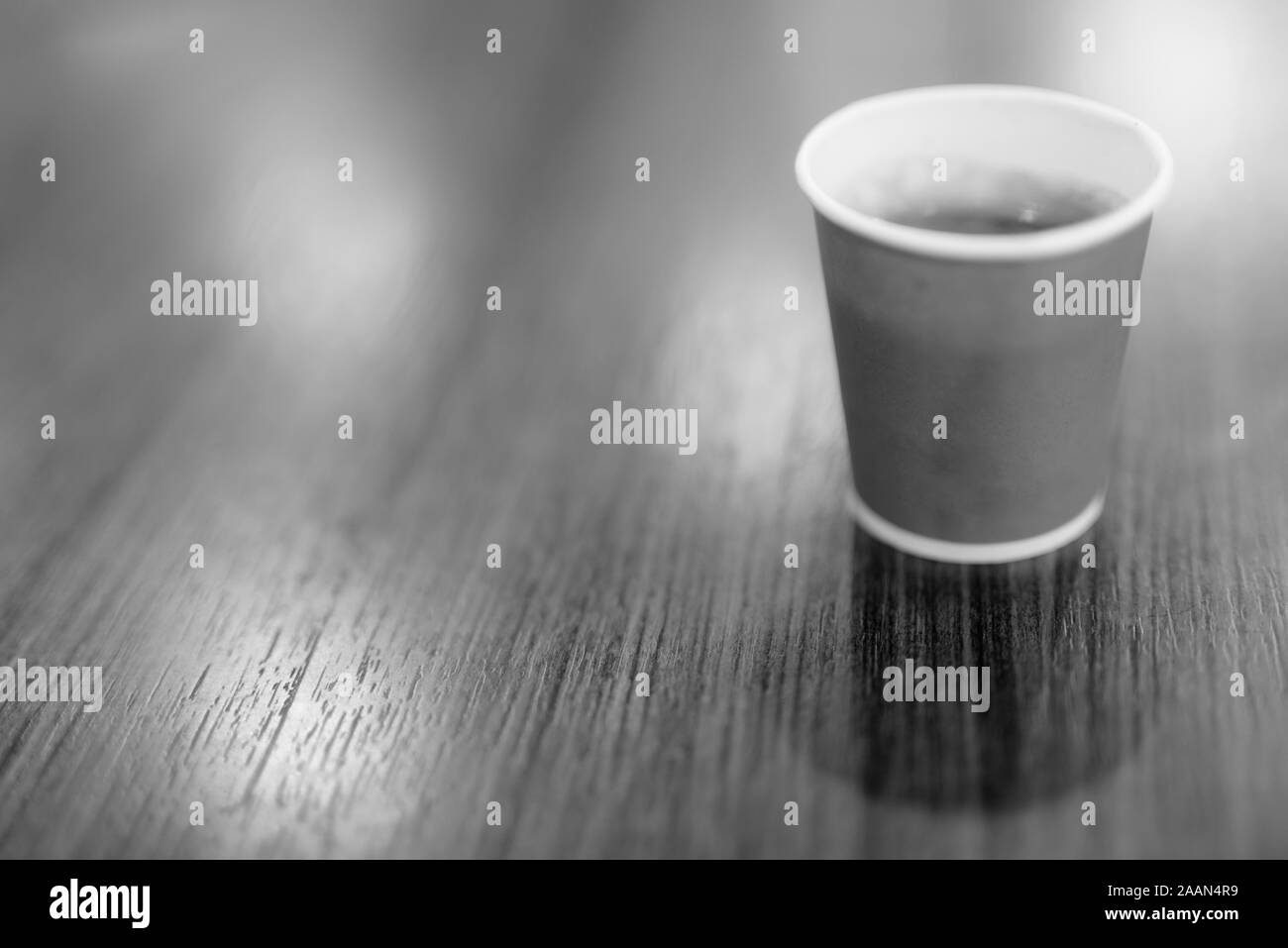 Café caliente en la taza de papel colocado sobre la mesa de madera en blanco y negro Foto de stock