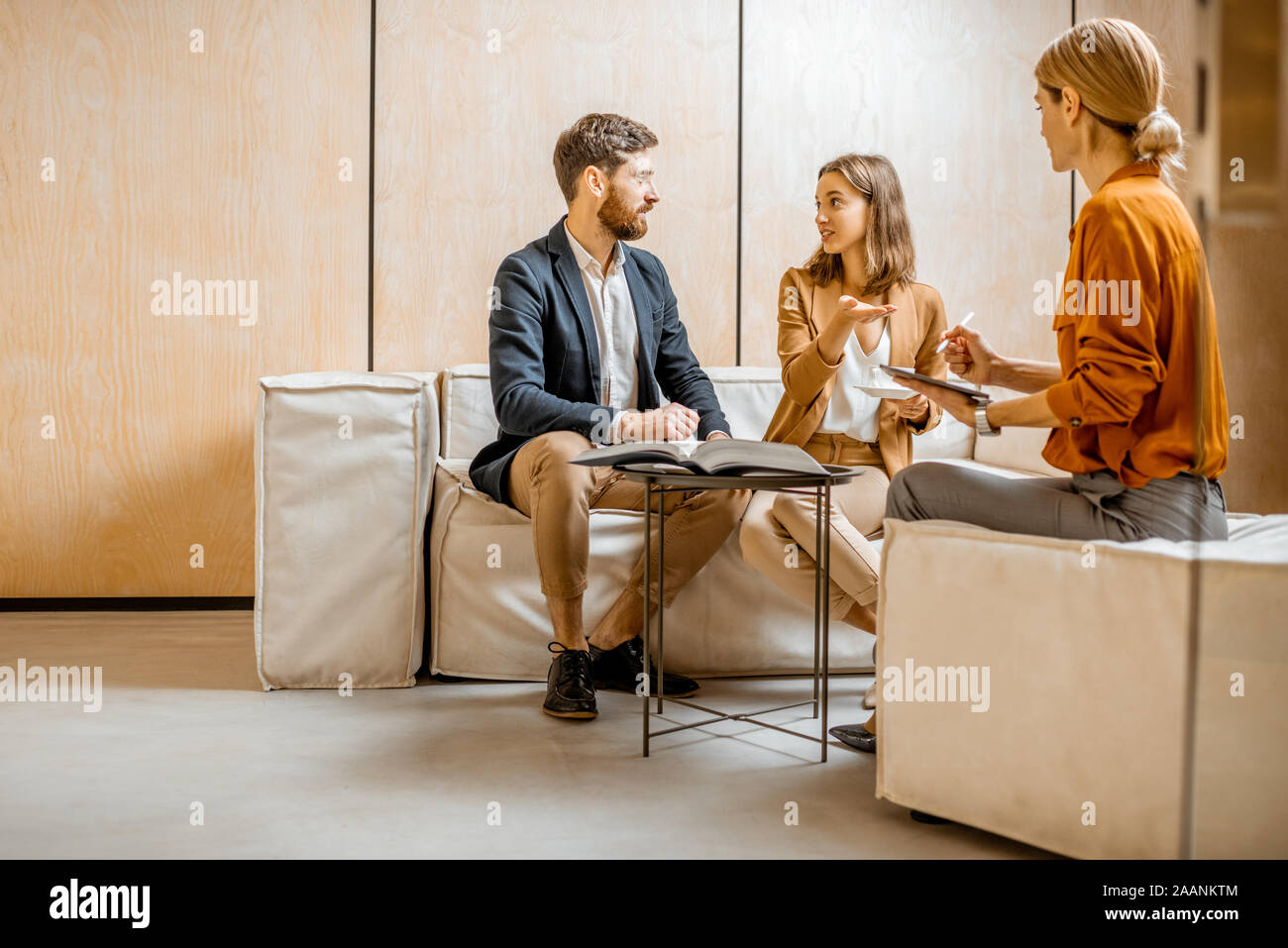 Pareja joven hablando con un gerente de ventas o agente inmobiliario, sentado en el cómodo sofá en la oficina Foto de stock