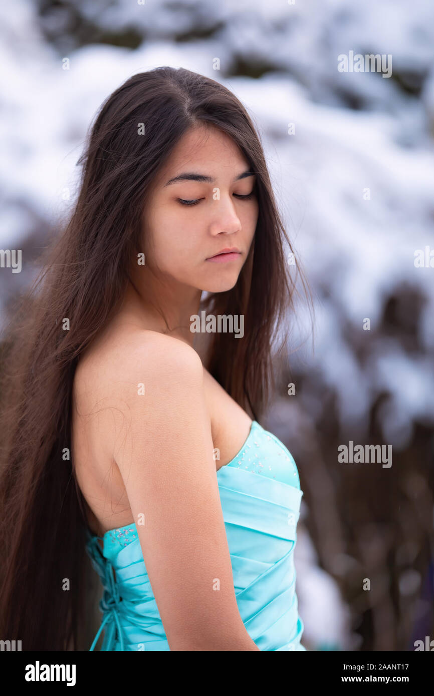 Birracial hermosa mujer joven con largo cabello negro vestido de azul aqua bata mientras está parado afuera en invierno Foto de stock