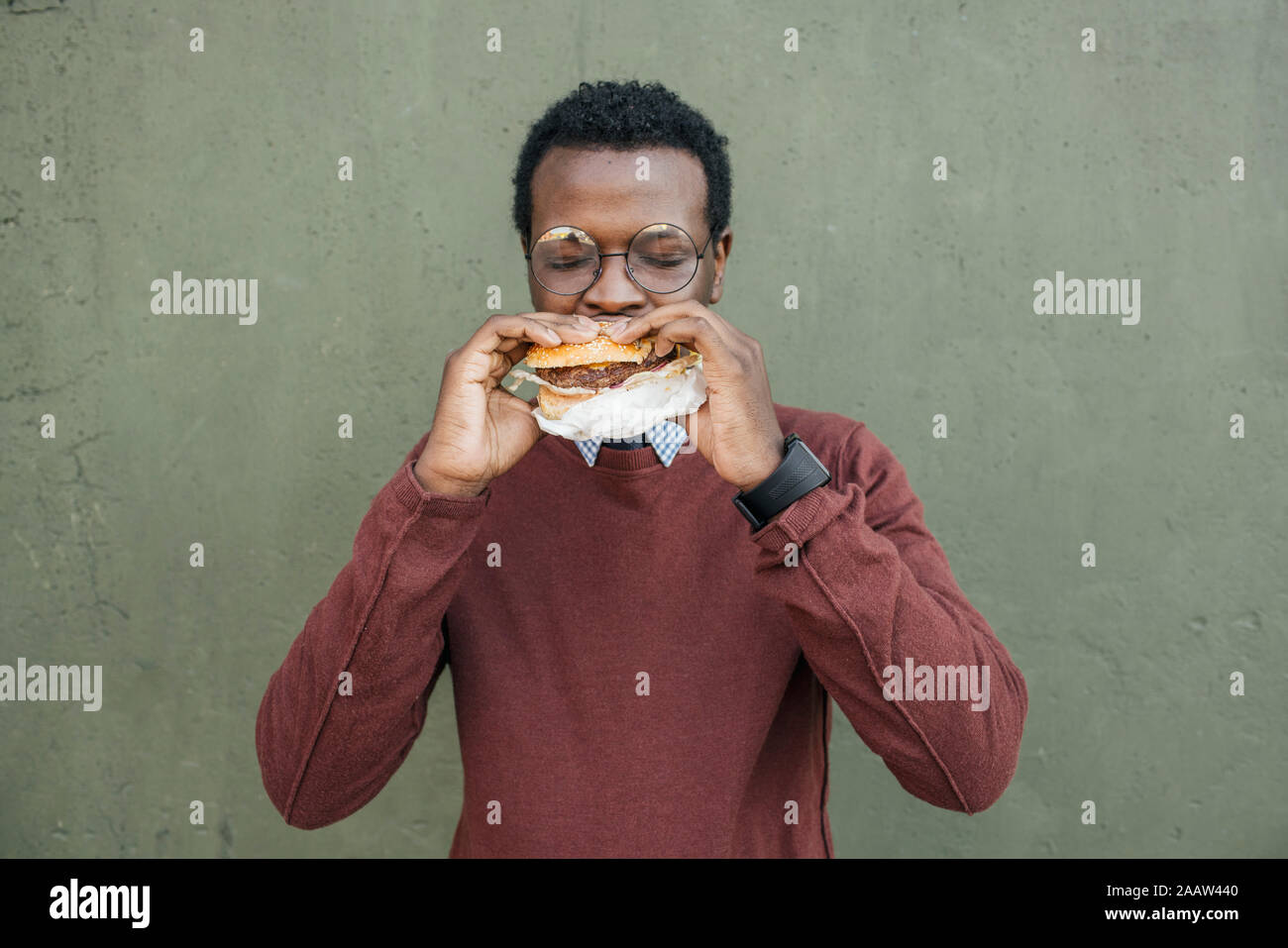 Joven comiendo una hamburguesa con queso, con los ojos cerrados Foto de stock
