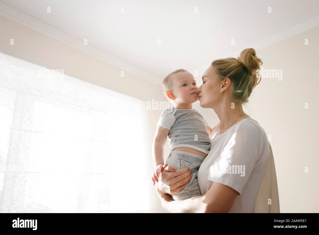 La madre abrazando a su pequeño muchacho cerca de la ventana Foto de stock