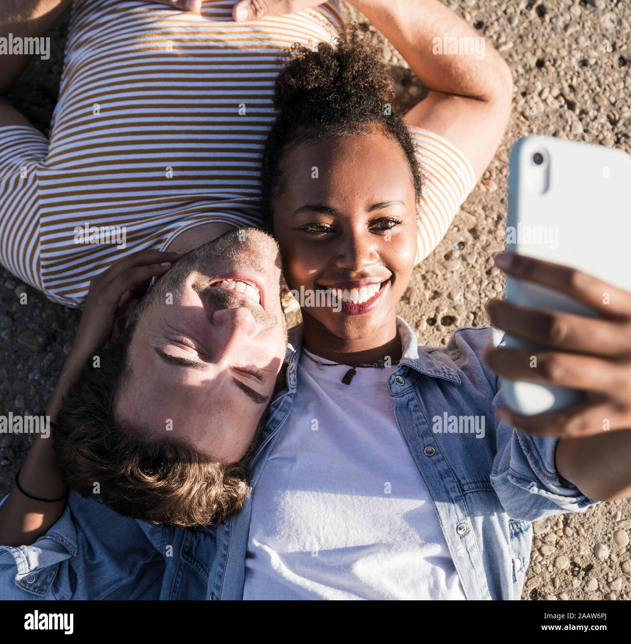 Feliz pareja joven acostado en el piso de concreto teniendo un selfie Foto de stock