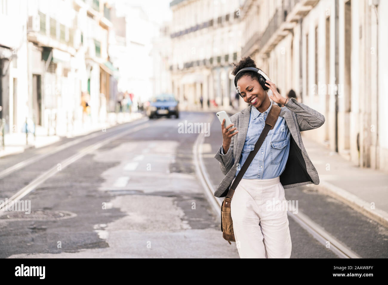 Mujer joven feliz con los auriculares y el teléfono móvil en la ciudad, Lisboa, Portugal Foto de stock