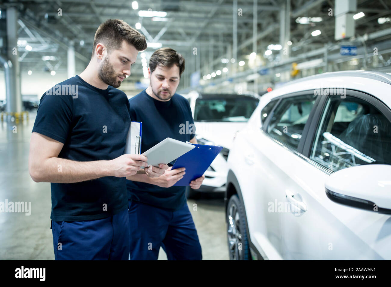Dos compañeros de trabajo en la moderna fábrica de coches utilizando el portapapeles y tablet Foto de stock