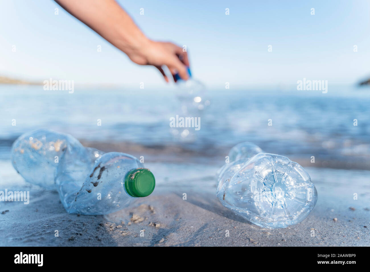 Mano recogiendo botellas vacías de plástico a orillas del mar Foto de stock