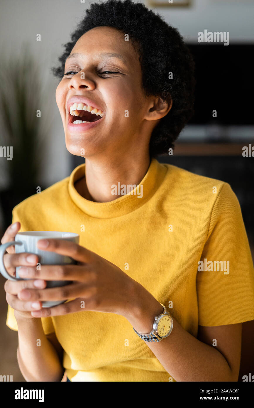 Laughing joven sosteniendo la taza en casa Foto de stock