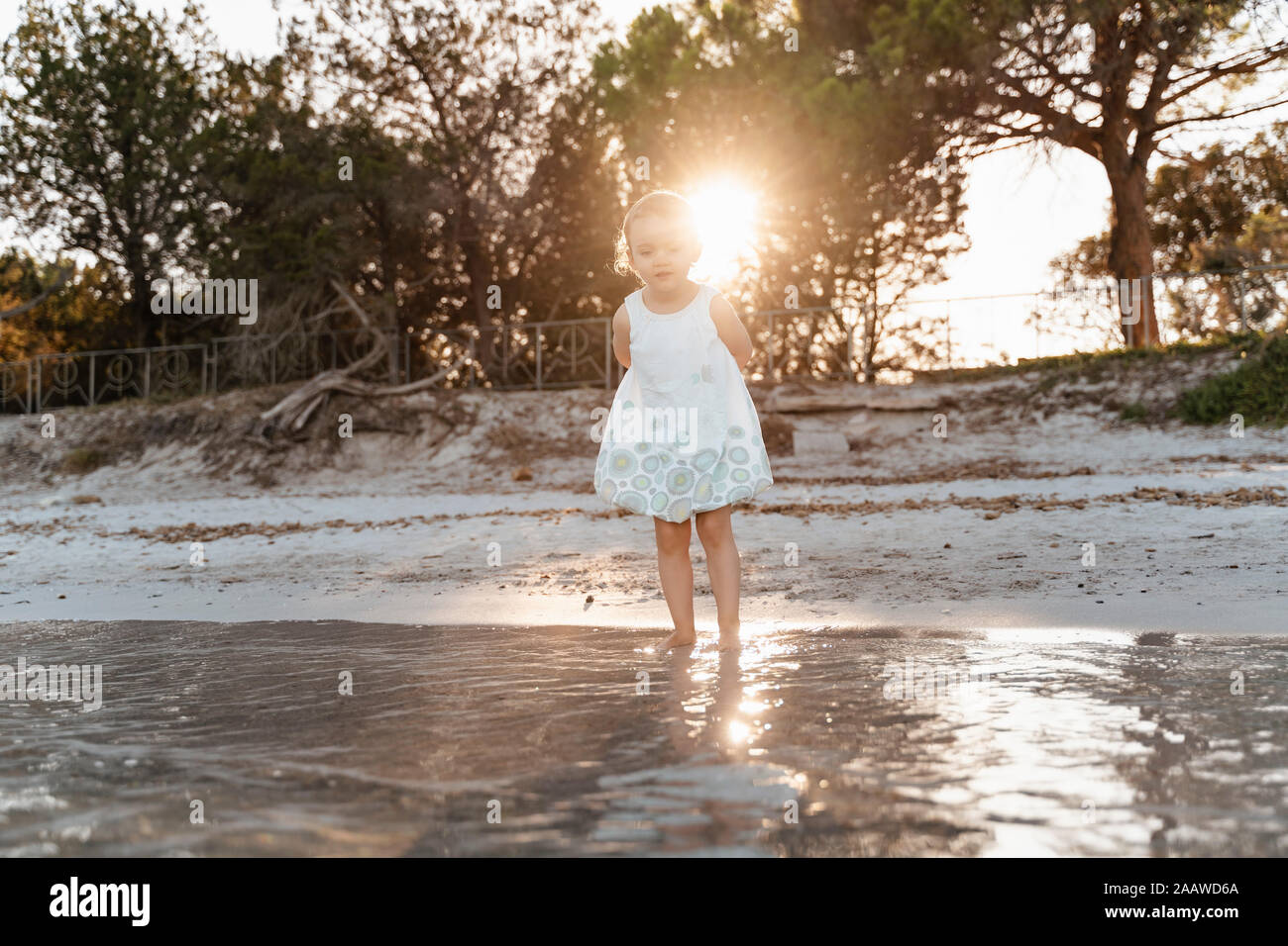 Lindo niño niña de pie en la playa en el atardecer. Foto de stock