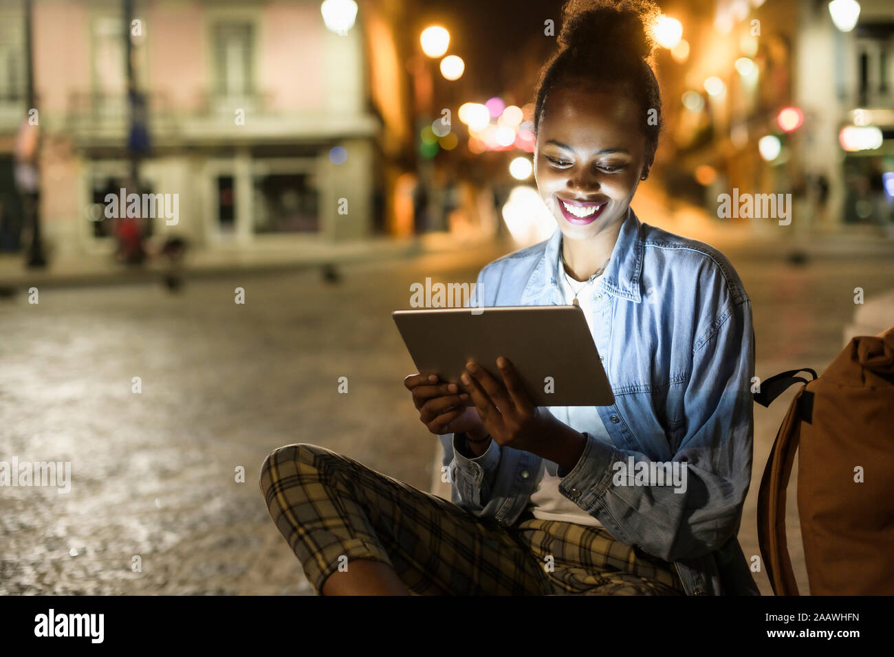 Retrato de mujer joven feliz con tableta digital en la ciudad por la noche, Lisboa, Portugal Foto de stock