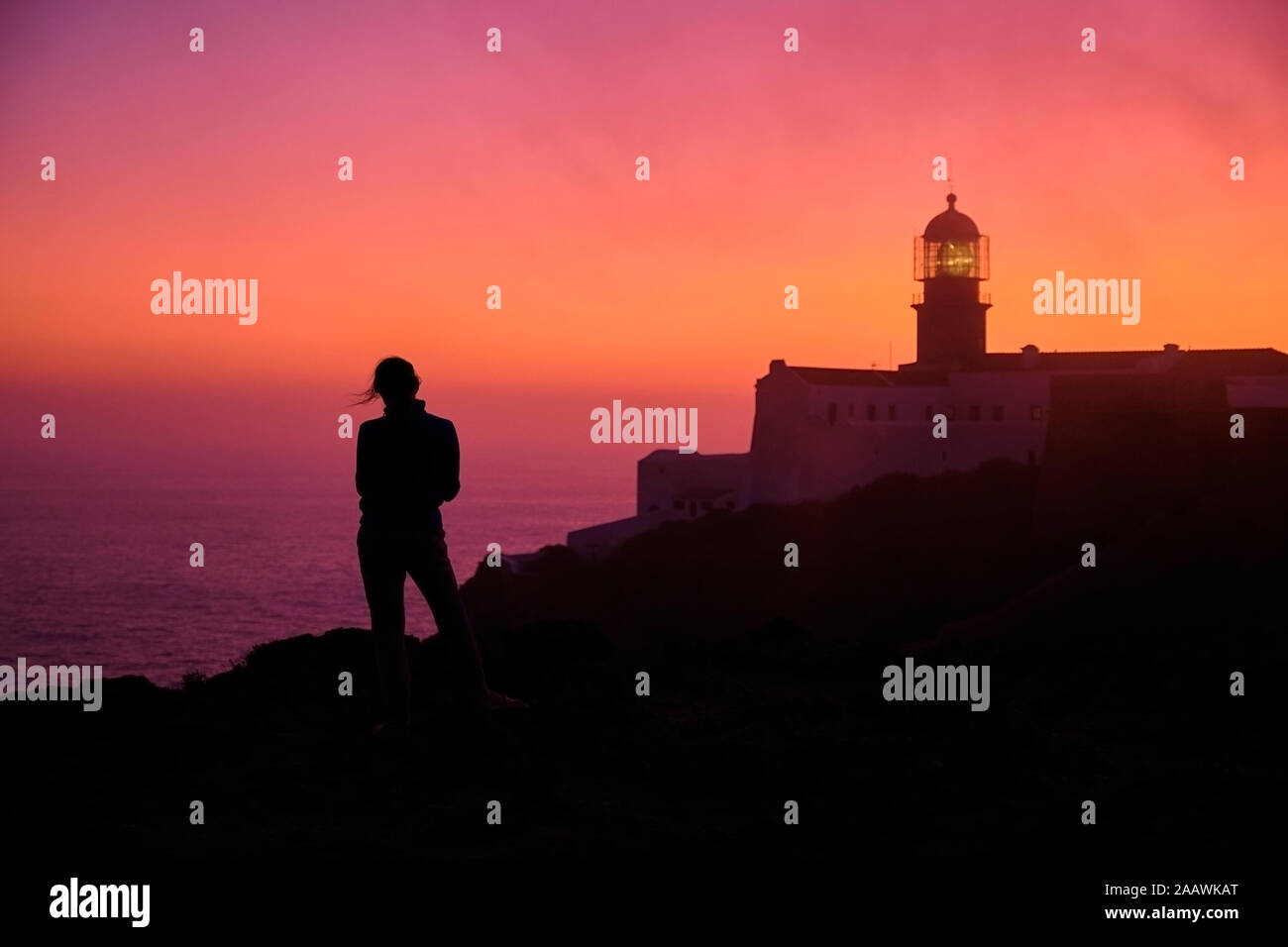 Portugal, Algarve, silueta de persona admirando la mar al amanecer con el Cabo de San Vicente lighthouse en segundo plano. Foto de stock