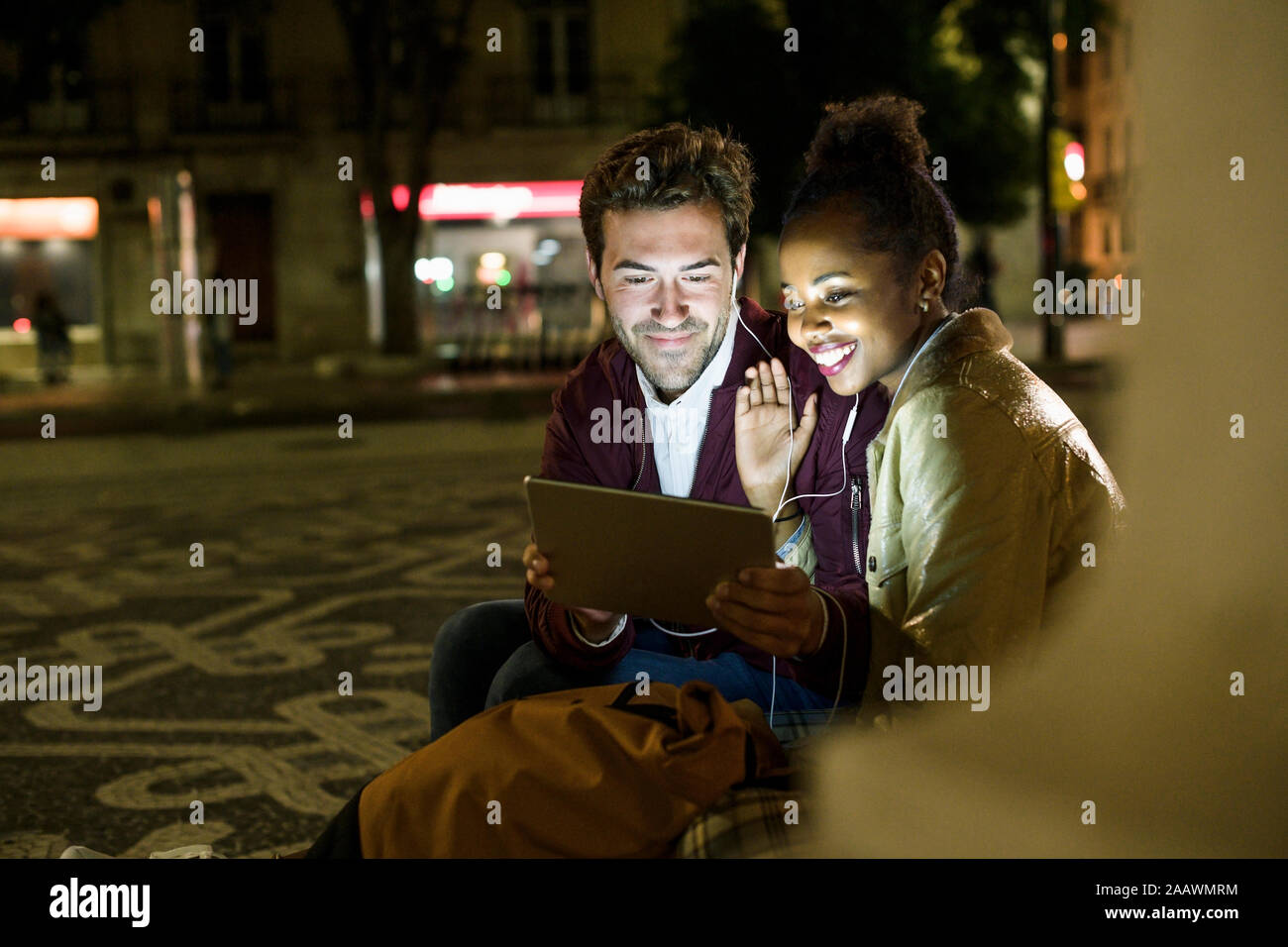 Retrato de sonriente joven pareja compartiendo auriculares mientras mira tableta digital, Lisboa, Portugal Foto de stock