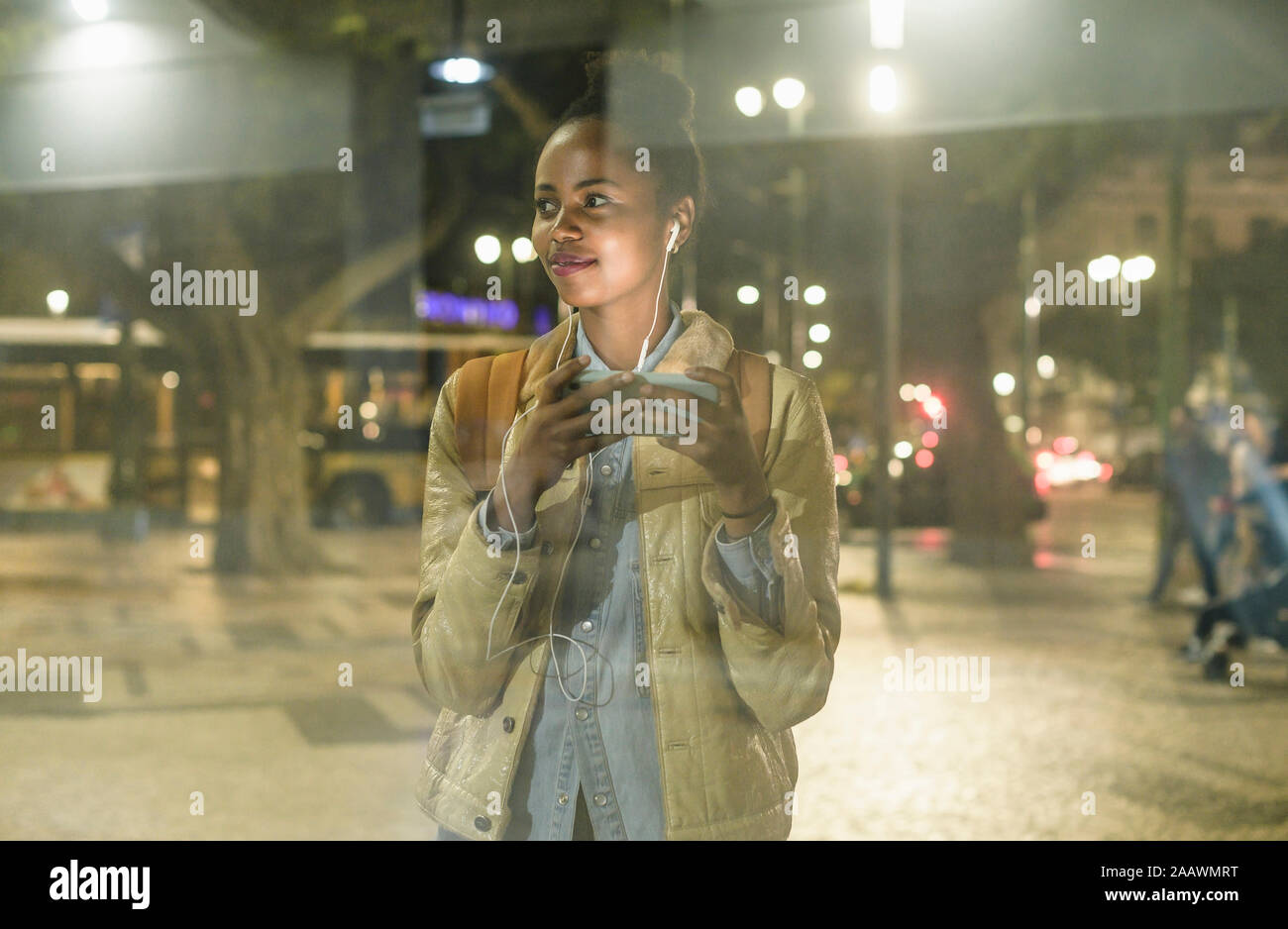Retrato de mujer sonriente con el smartphone y auriculares viendo algo, Lisboa, Portugal Foto de stock
