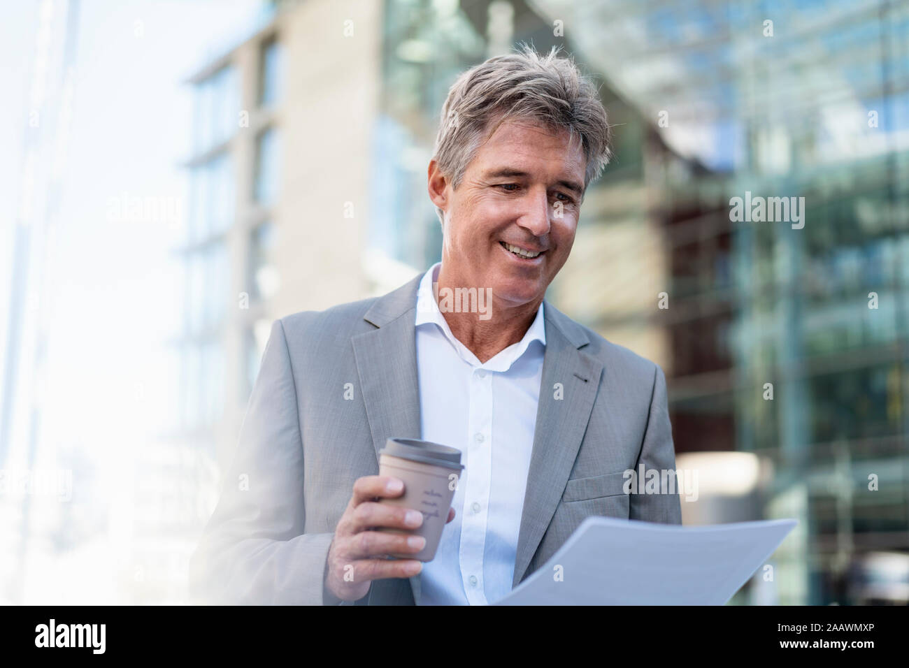 Sonriente empresario maduro con café para llevar revisar documentos en la ciudad Foto de stock