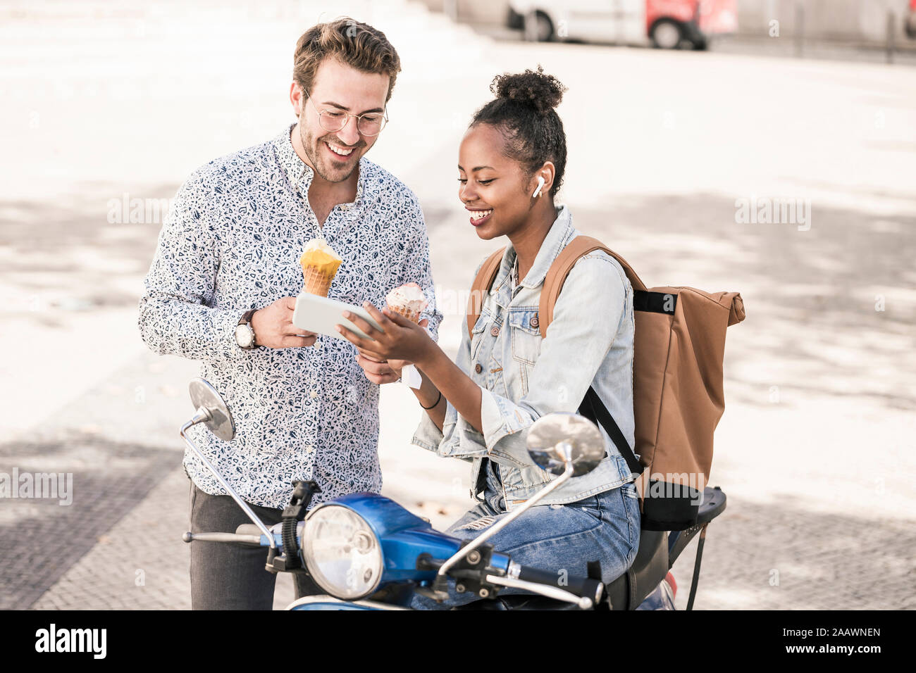 Feliz pareja joven con motor scooter y helados a través de teléfono móvil en la ciudad, Lisboa, Portugal Foto de stock