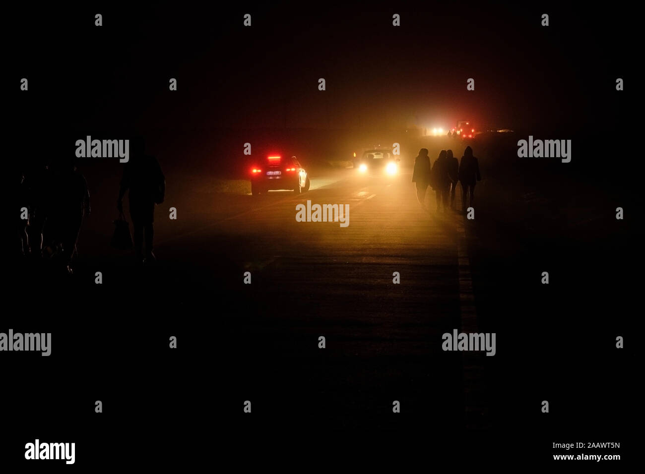 Portugal, Algarve, autos pasando las siluetas de cuatro personas caminando a lo largo de la carretera en el Cabo de San Vicente en la noche Foto de stock