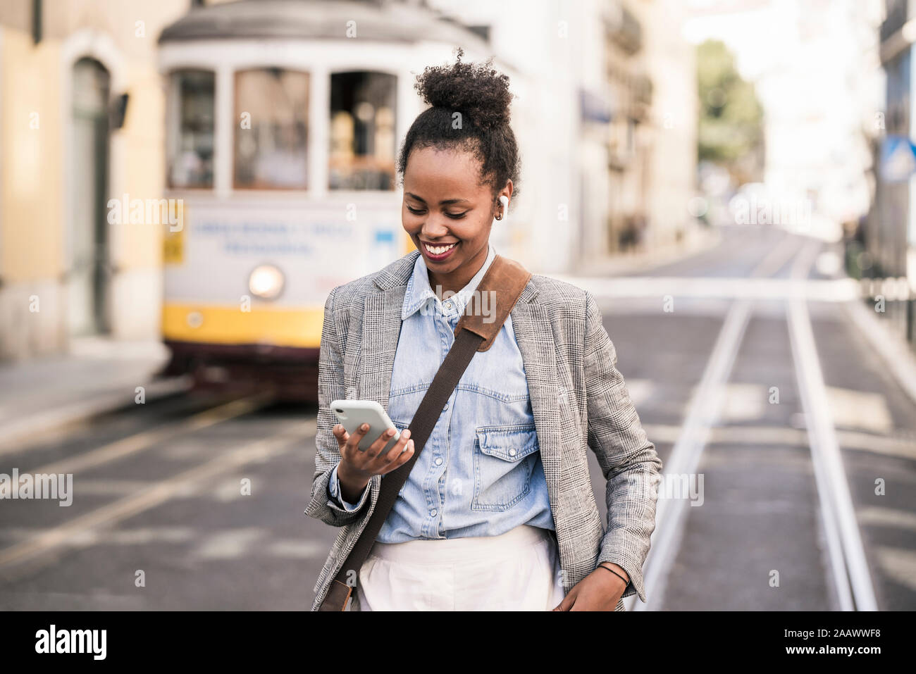 Mujer sonriente con auriculares y el teléfono móvil en la ciudad, Lisboa, Portugal Foto de stock