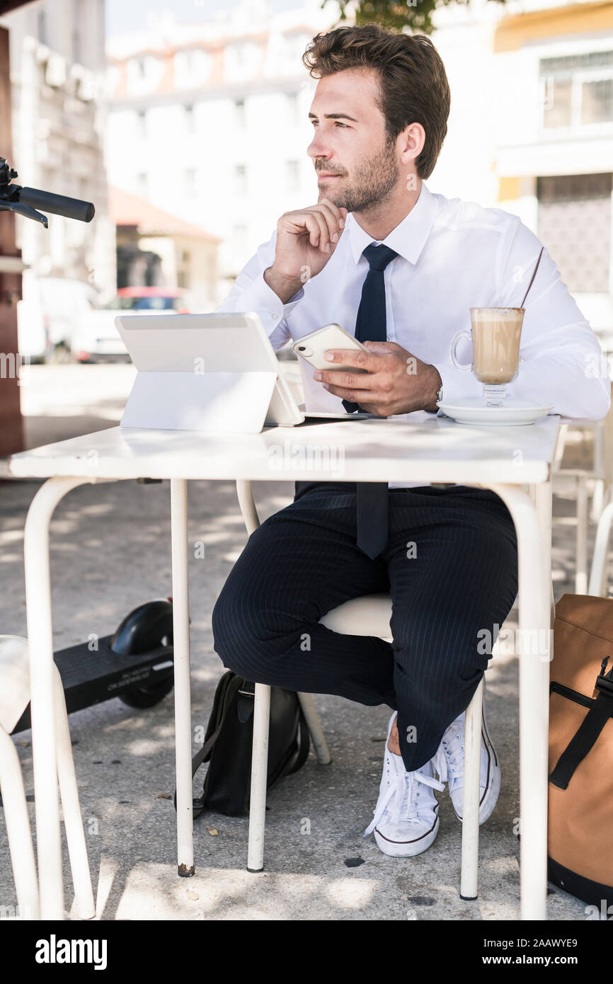 Joven empresario utilizando tablet y teléfono móvil en una cafetería de la ciudad, Lisboa, Portugal Foto de stock