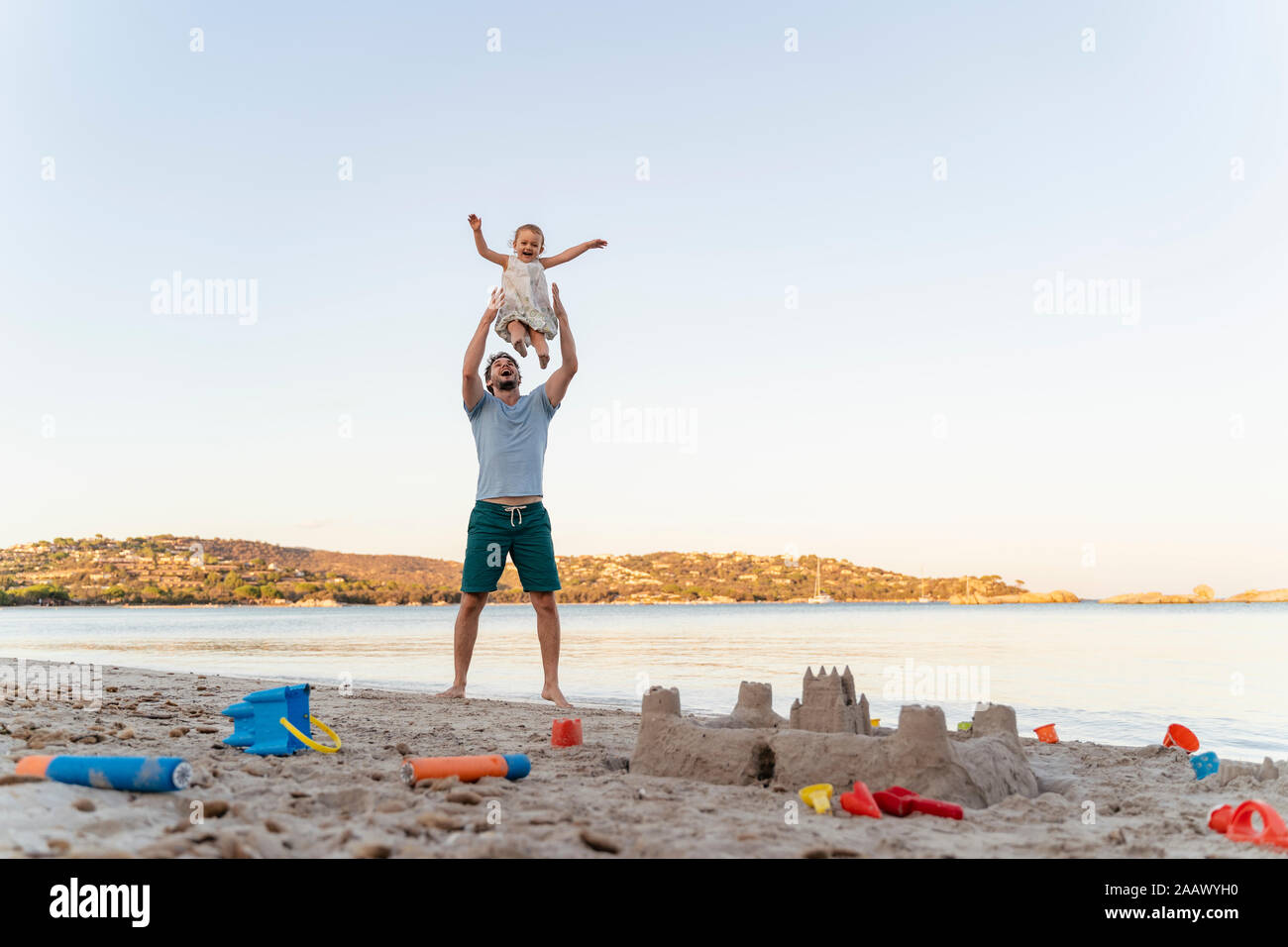 Castillo de arena y feliz padre levantando la hija en la playa Foto de stock