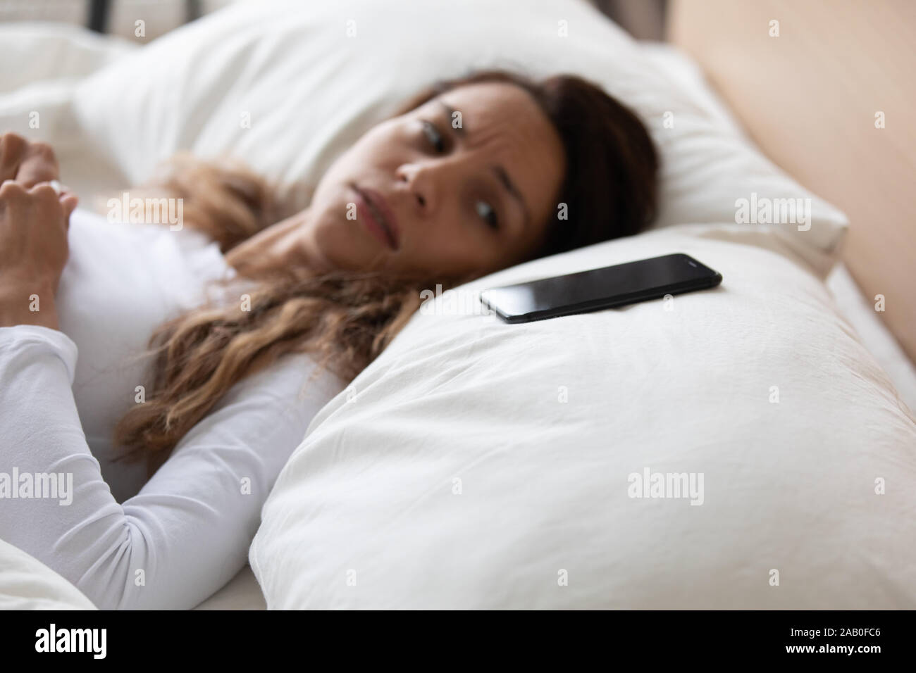 Mujer asustada acostado en la cama mirando en el smartphone se siente Foto de stock