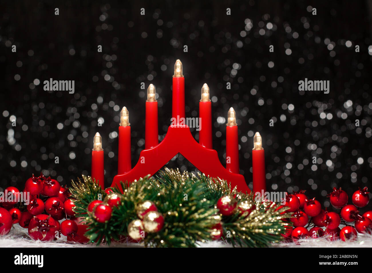 Puente de luces de velas rojas de Navidad, bayas rojas de izquierda y derecha sitio y Navidad verde corona redonda en color oro con las puntas sobre fondo oscuro Foto de stock