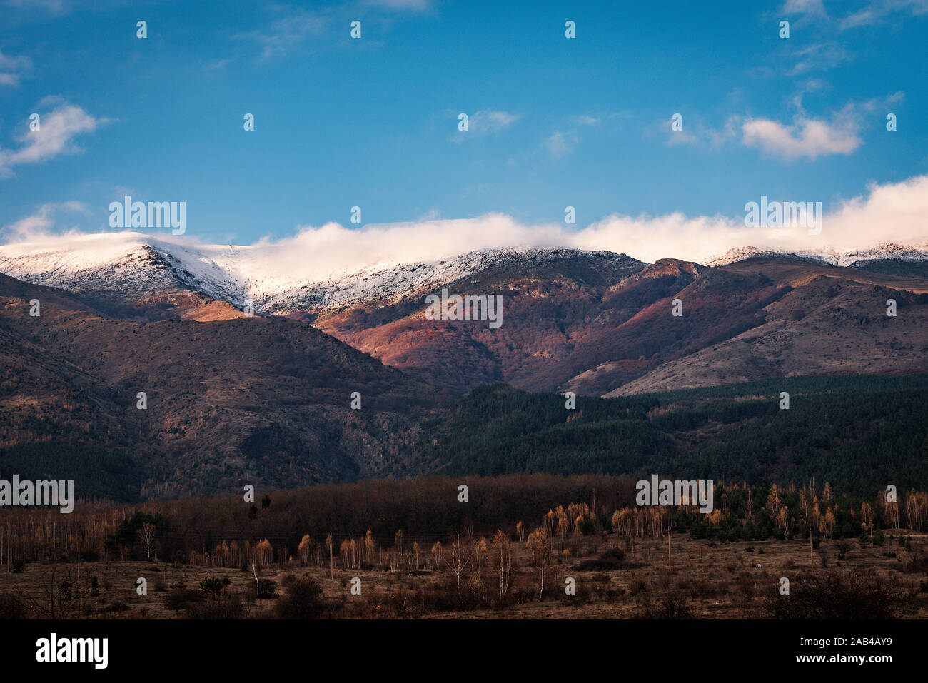 Las últimas horas del día con las montañas nevadas con blancas nubes hinchadas y cielo azul Foto de stock