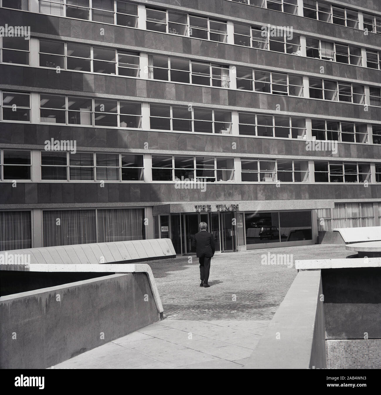 1960, historcial, el hombre en un vestíbulo caminando hacia un edificio moderno de hormigón construido el edificio de oficinas de la época, la casa de el diario británico "The Times", de Londres, Inglaterra, Reino Unido. Foto de stock