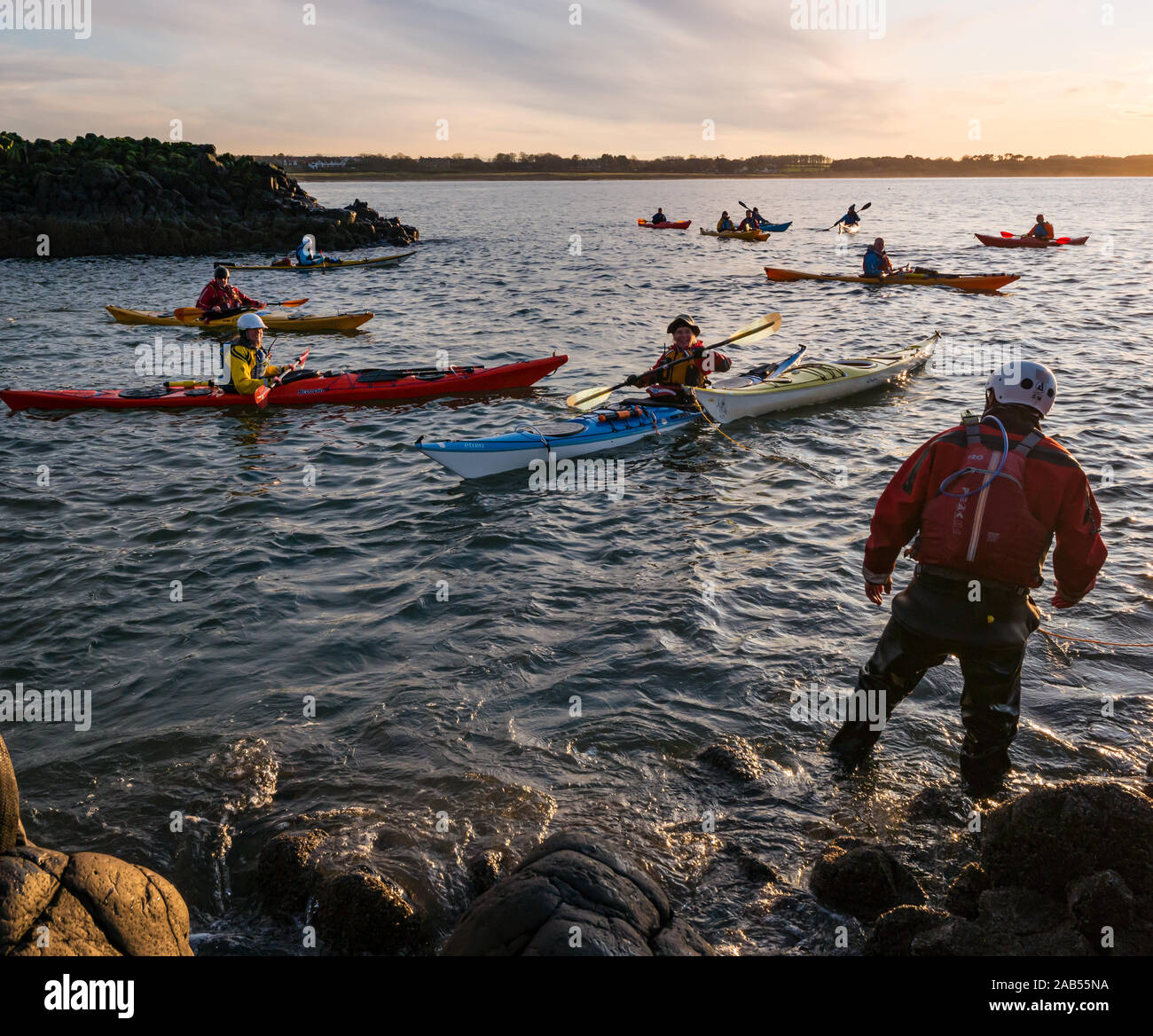 Kayak de Mar Club Lothian palistas se preparan para abandonar desde la orilla rocosa con kayaks, al atardecer, la isla de cordero, Firth of Forth, Escocia, Reino Unido Foto de stock