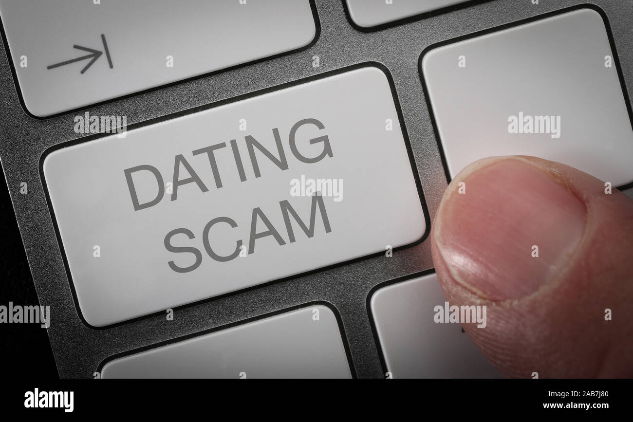Un hombre presionando una tecla en un teclado de ordenador con las palabras dating scam. Online dating estafa concepto imagen. Foto de stock