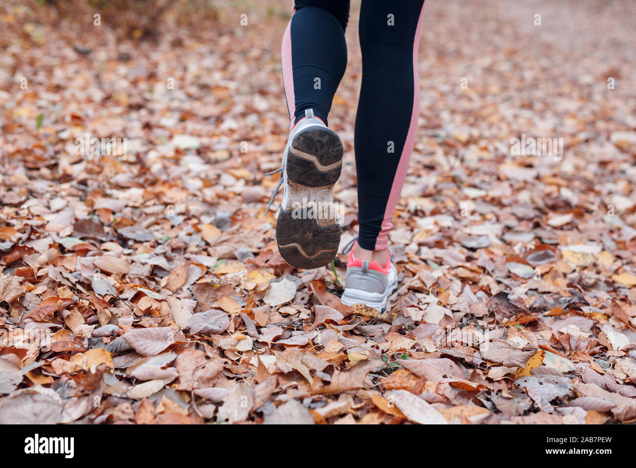 Cerca de los pies de un corredor corriendo en hojas de otoño en el parque Foto de stock