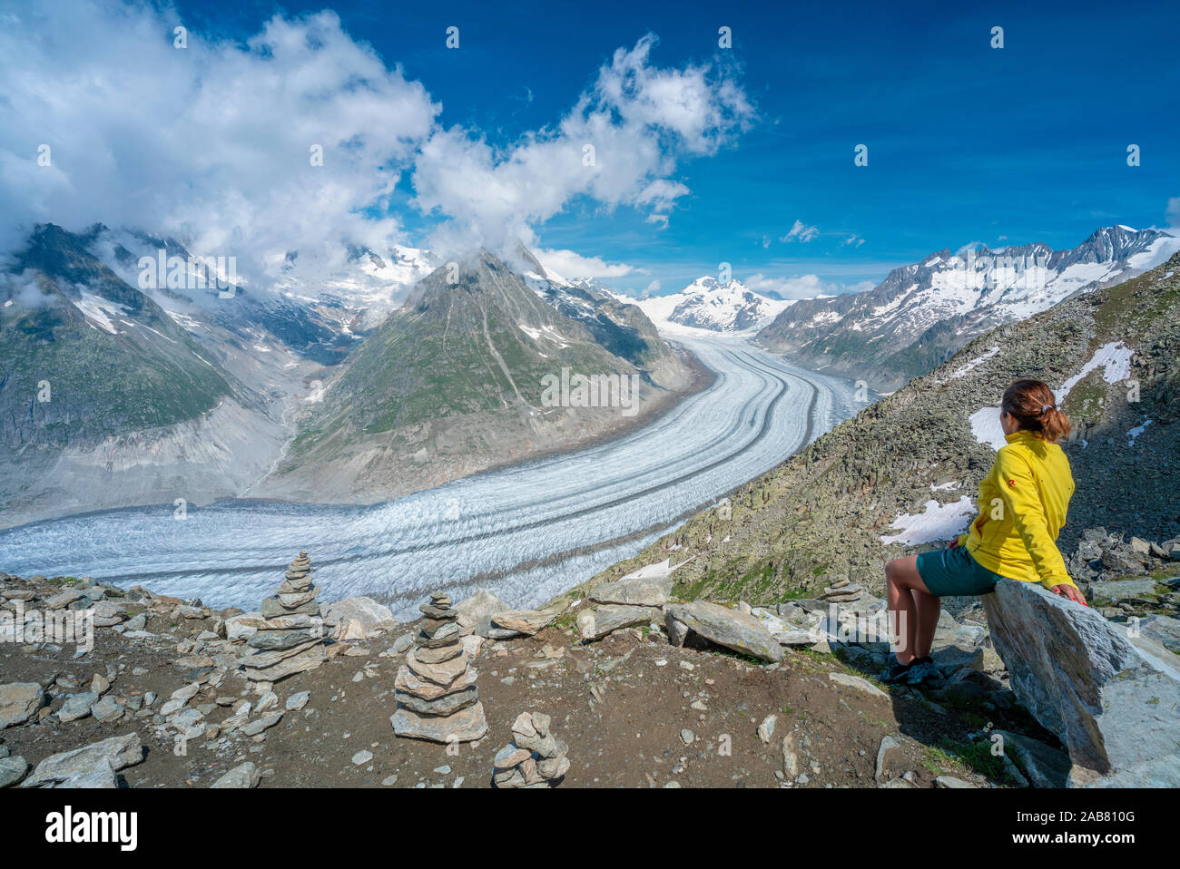 Vista lateral de la mujer sentada sobre las rocas, admirando el Glaciar Aletsch desde el punto de vista Eggishorn, Alpes Berneses, cantón de Valais, Suiza, Europa Foto de stock