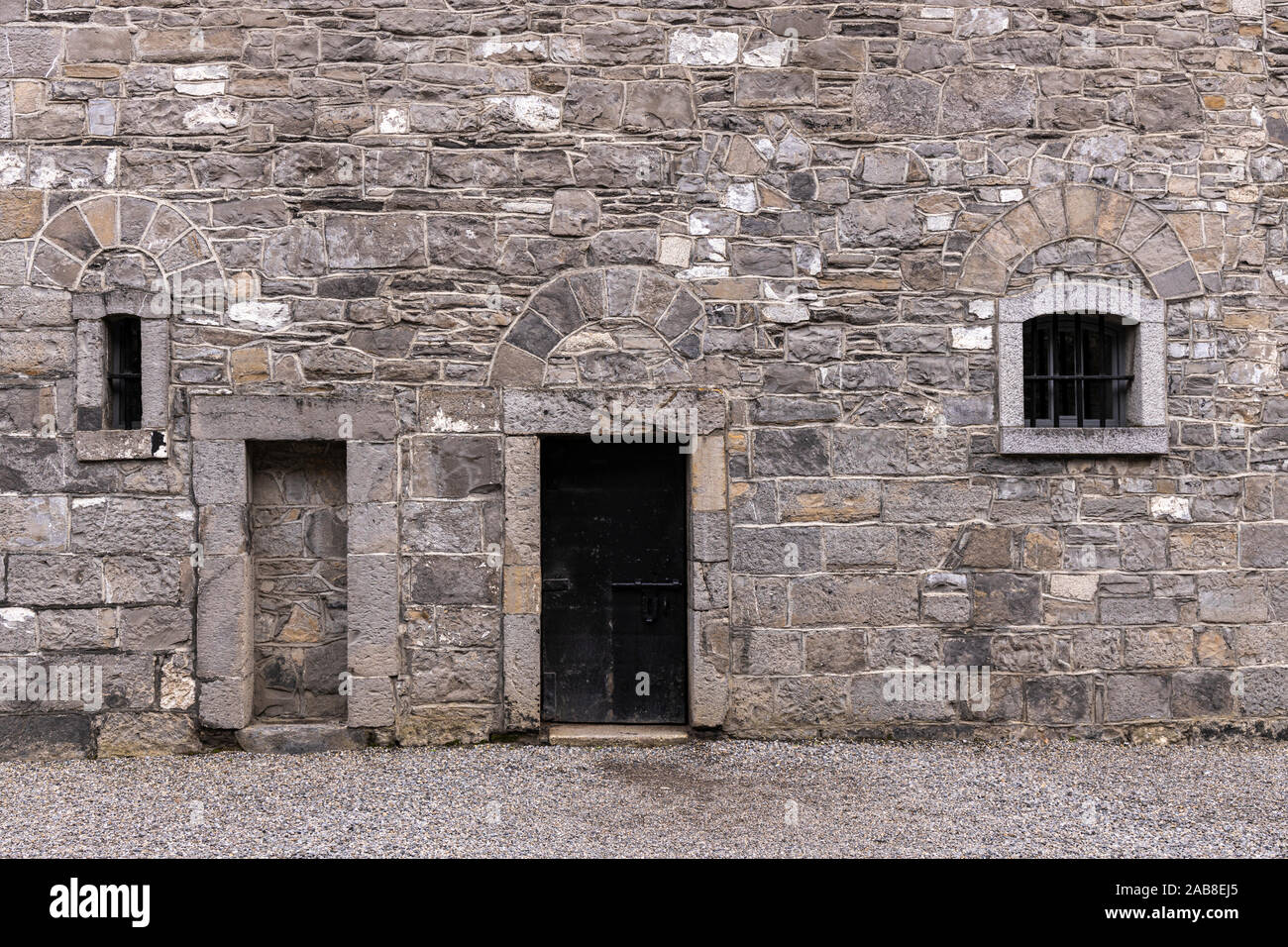 Muro de piedra gris con puerta y ventanas que dan a un patio interior en la Cárcel de Kilmainham, Dublín, Irlanda Foto de stock