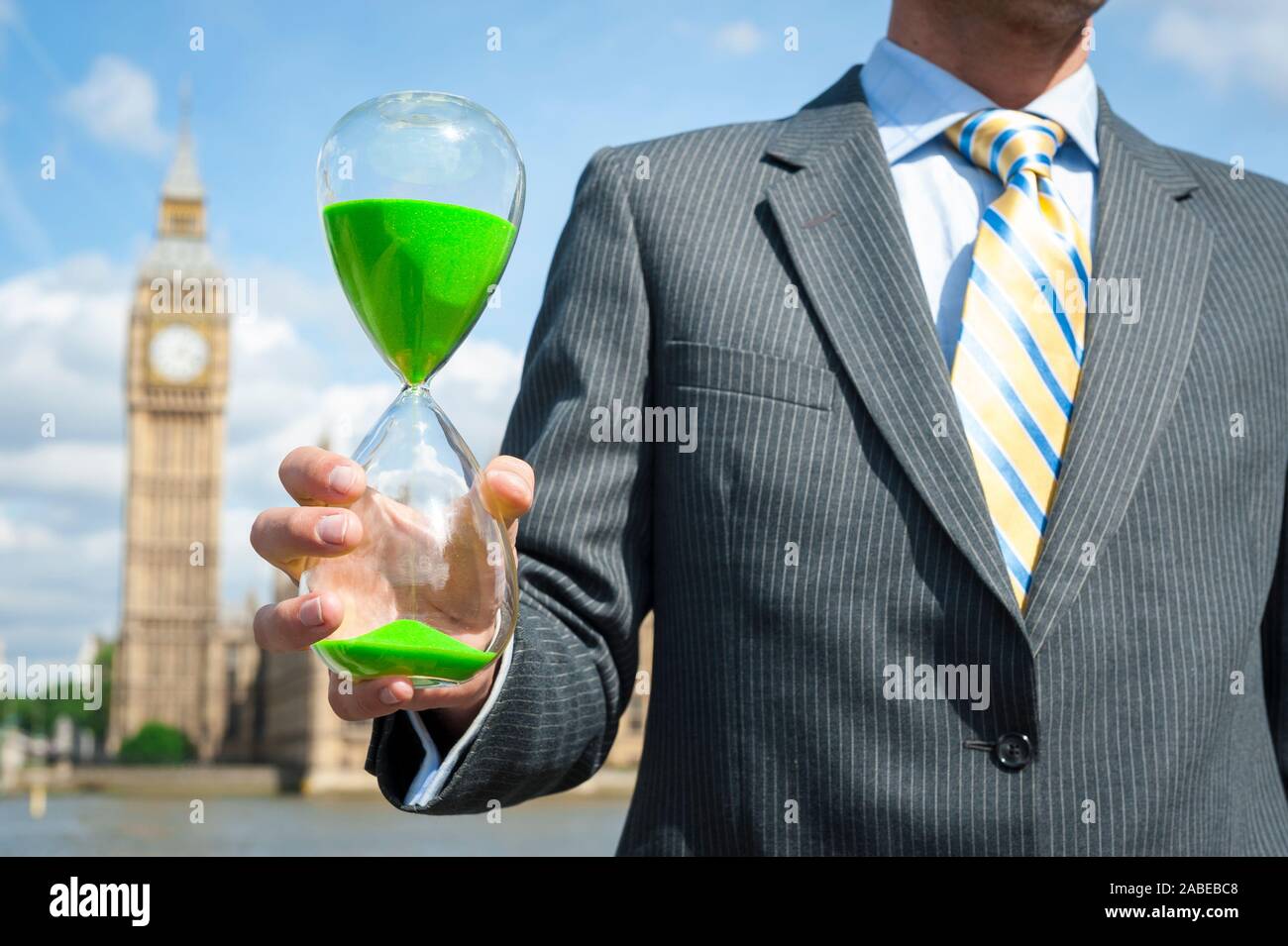 Hombre de negocios británico sosteniendo un reloj de arena el cambio climático verde delante del Big Ben y las Casas del Parlamento de Westminster en Londres, Reino Unido Foto de stock