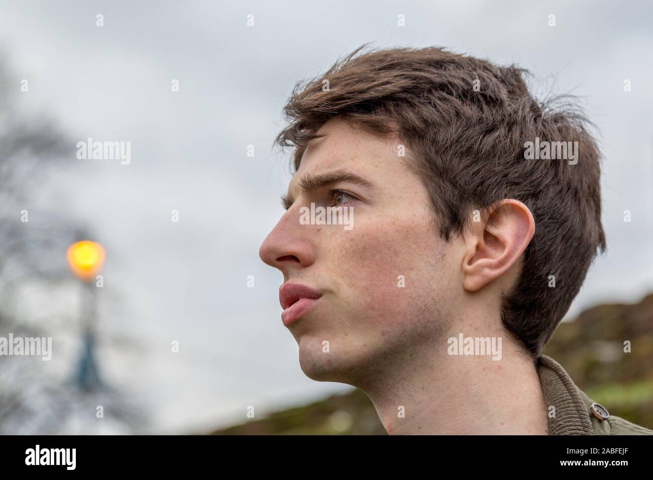 Un hombre joven en su adolescencia o principios del veinte stands al aire libre con una grave expresión centrada como se ve en la distancia. Foto de stock