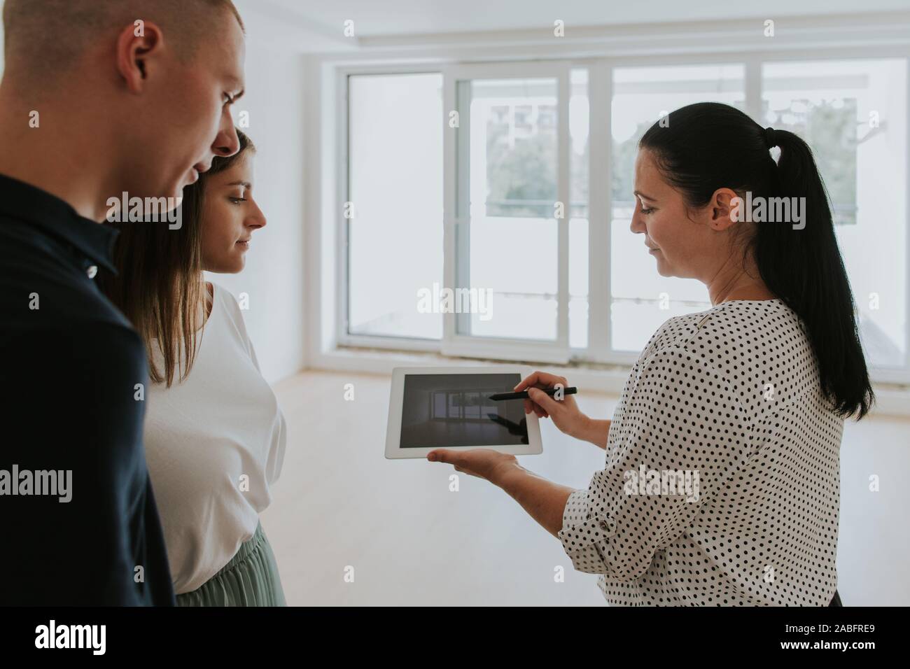 Agente inmobiliario mediante tableta digital mostrando pareja joven nueva casa Foto de stock
