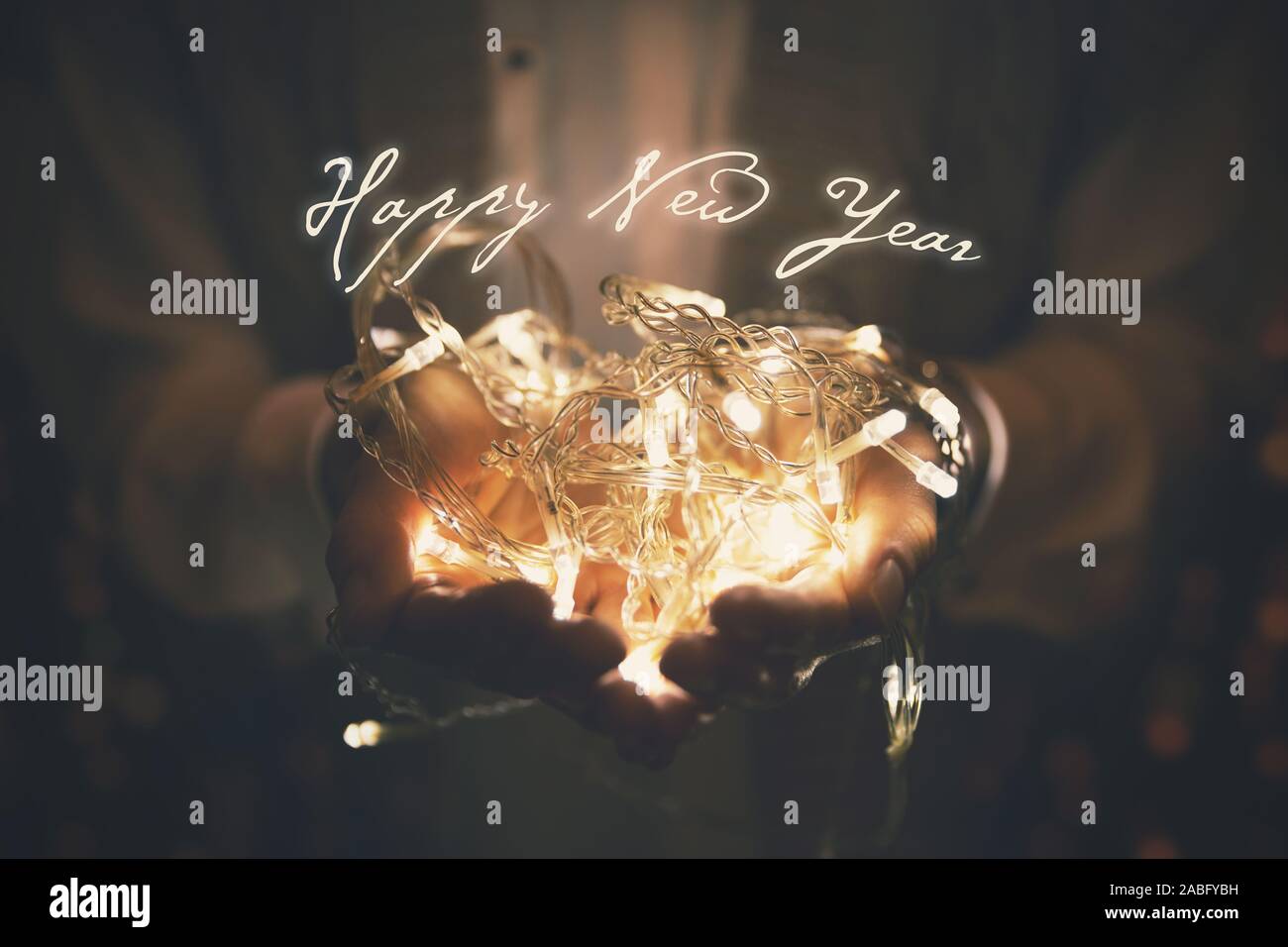 Feliz año nuevo - Tarjeta de felicitación guirnalda de luces LED que se iluminan en manos de mujer Foto de stock