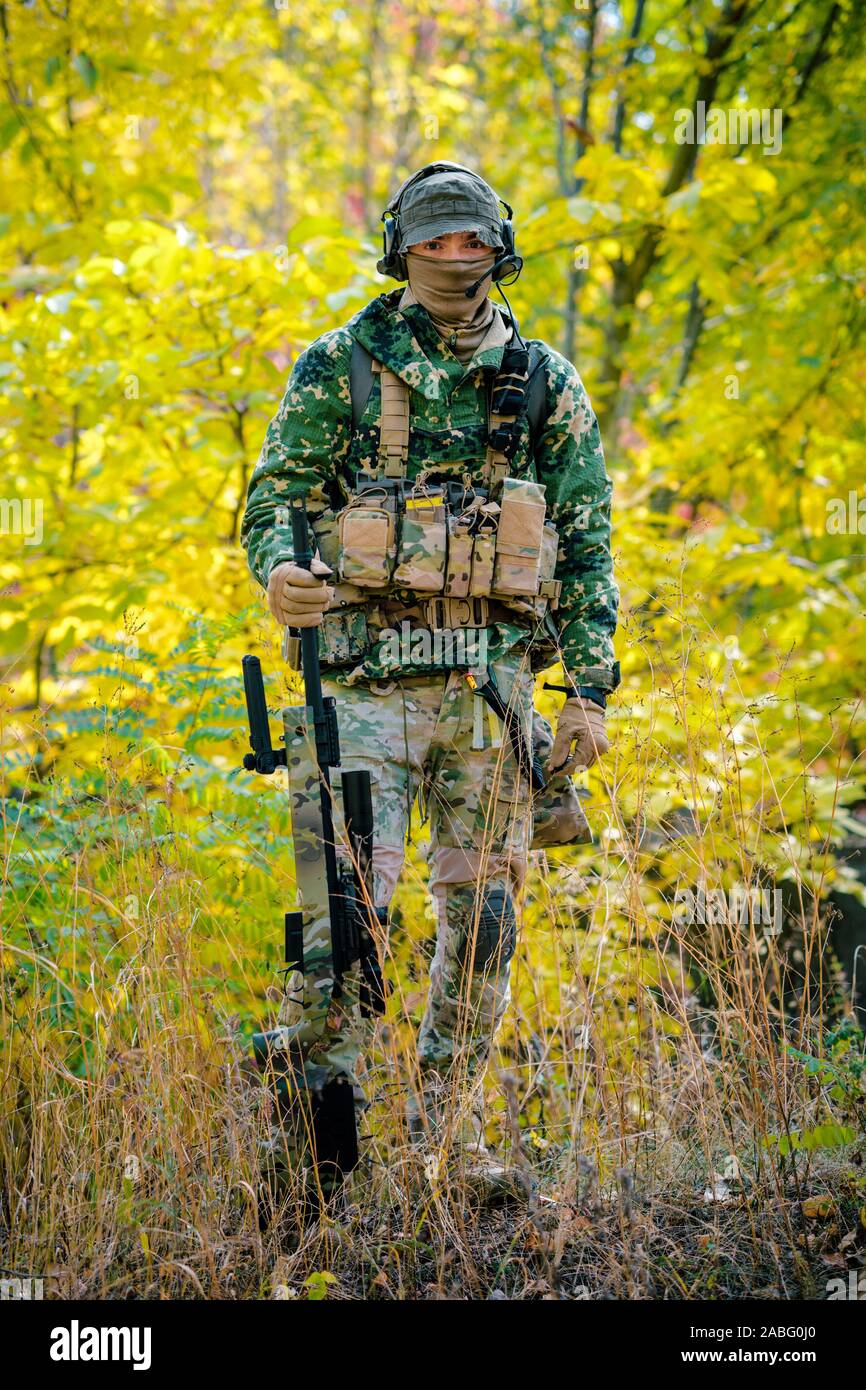 Airsoft hombre uniformado mantenga un rifle de francotirador en bosque  amarillo como telón de fondo. Vista lateral Fotografía de stock - Alamy