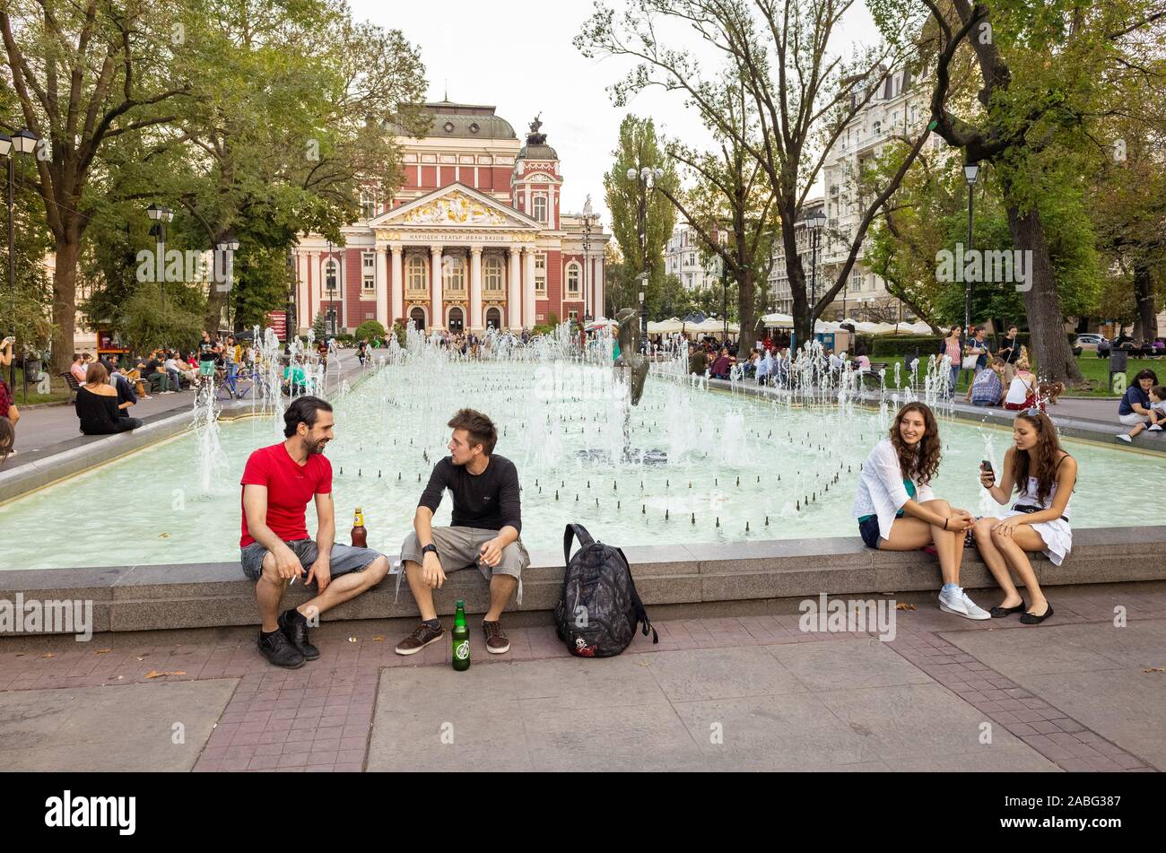 Jóvenes que se encuentran en el parque City Garden, frente al Teatro Nacional Ivan Vazov, Sofía, Bulgaria Foto de stock
