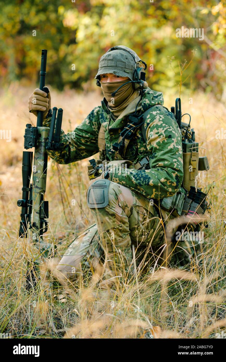 Airsoft hombre uniformado con un rifle de francotirador, que acechan en el  césped en el fondo del bosque. Foto vertical Fotografía de stock - Alamy