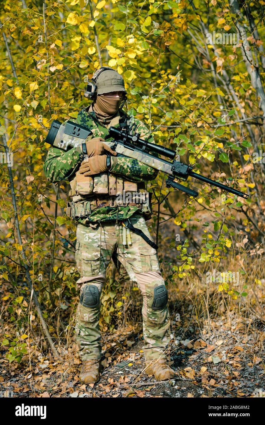 Airsoft hombre uniformado mantenga un rifle de francotirador en bosque  amarillo como telón de fondo. Vista lateral Fotografía de stock - Alamy