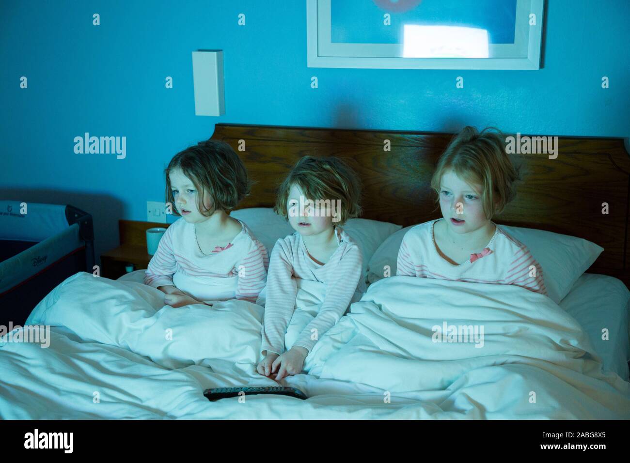 Tres niñas, con edades entre 6, 4 y 8 años - en una cama de hotel viendo la televisión programa infantil de la televisión en el hotel mientras está de vacaciones, después de despertarse por la mañana, pero igualmente podría ser ilustrativo de ir a la cama por la noche y mirar la televisión(105). Foto de stock