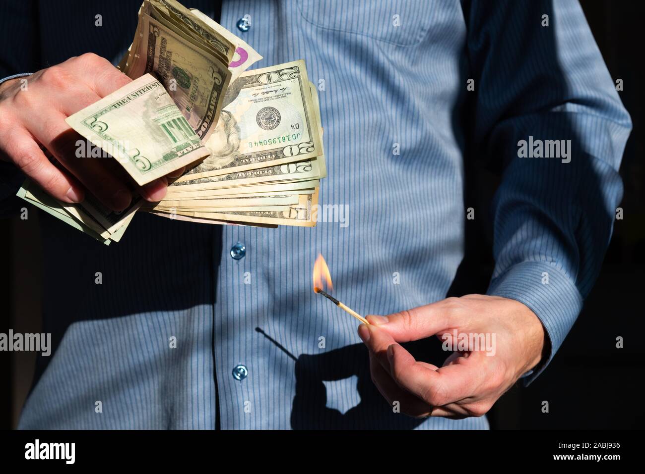 Close-up de hombre sujetando cerilla ardiendo cerca de gran puñado de dólares americanos Foto de stock