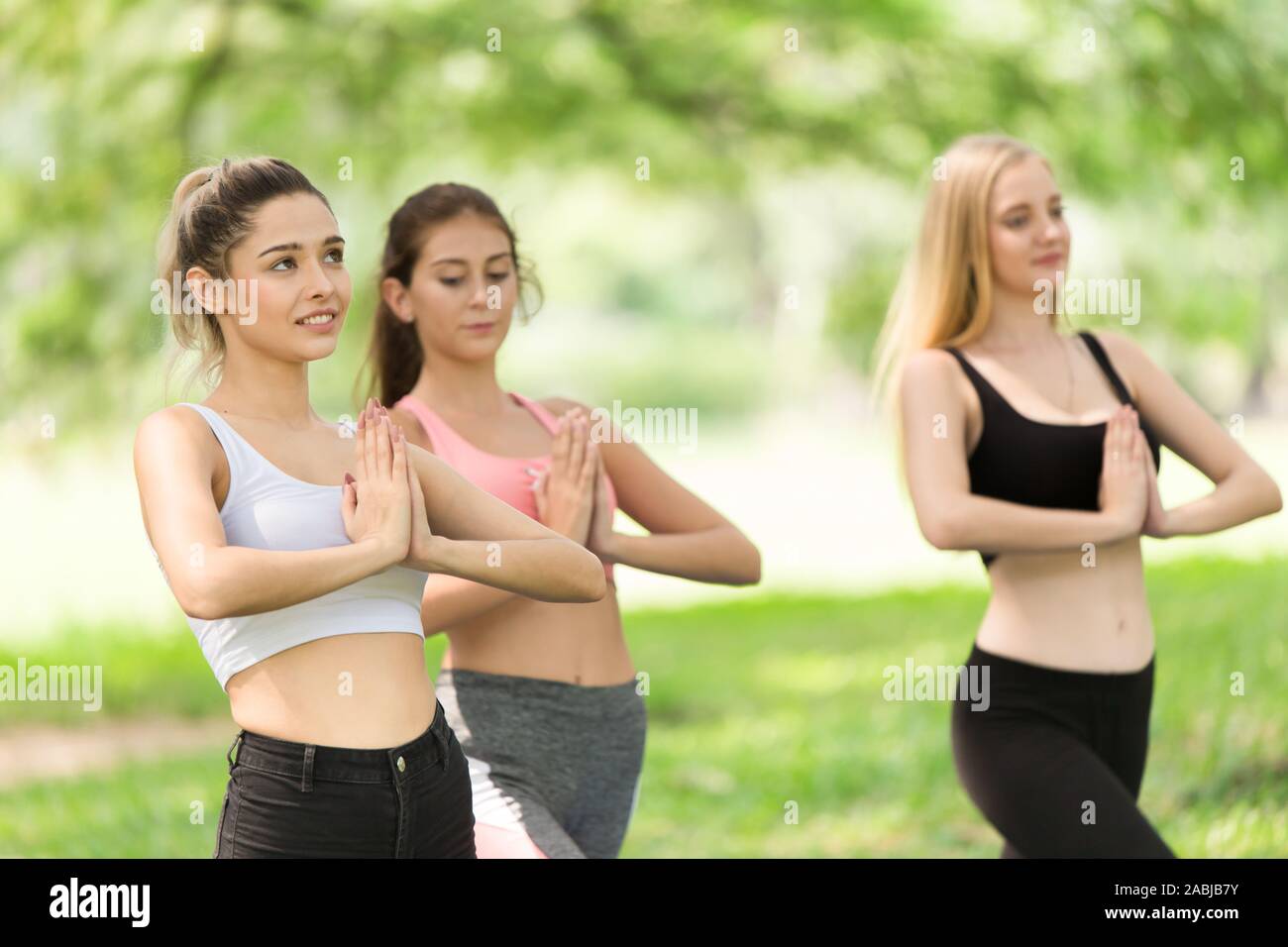 Hermosa niña modelo adolescente hacer yoga grupo de sano en el parque al aire libre. equilibrio en bipedestación la postura de loto. Foto de stock