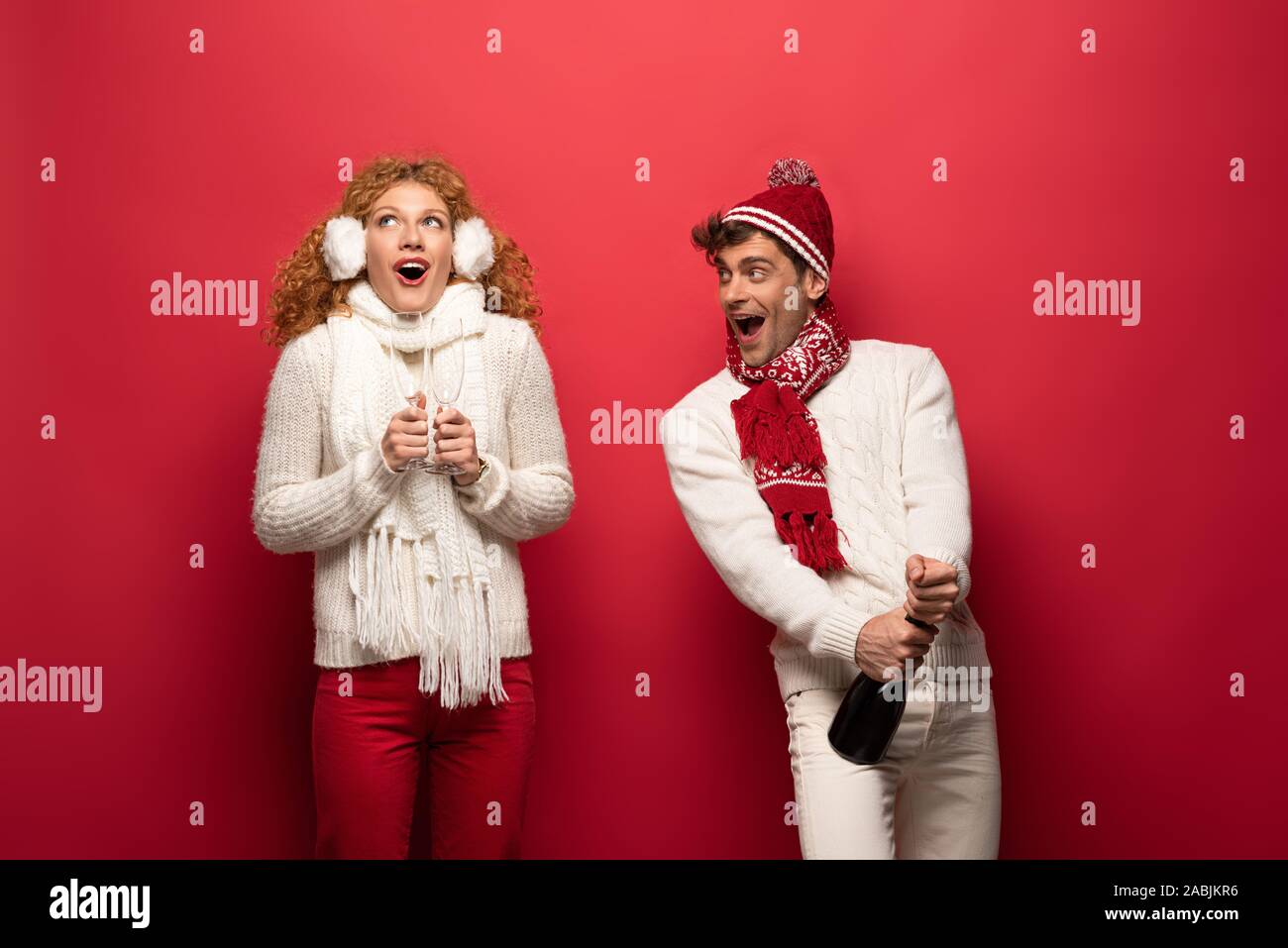 Pareja excitado en invierno outfit sosteniendo el champán para celebrar la  Navidad, sobre rojo Fotografía de stock - Alamy