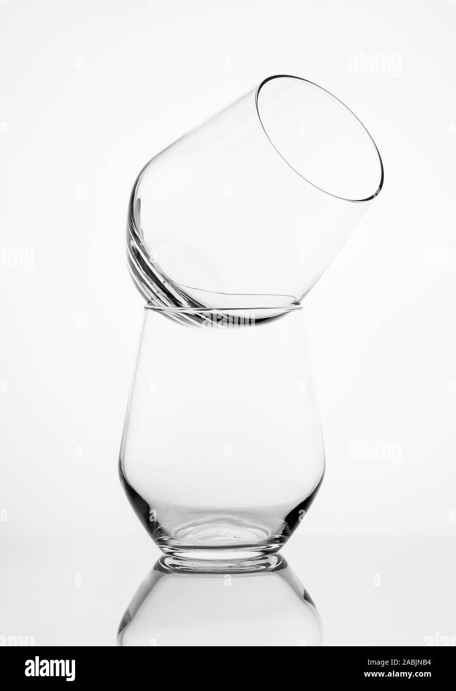 Dos vasos de whisky en pie como una pirámide sobre una superficie de espejo oscuro y un fondo blanco. Foto de stock