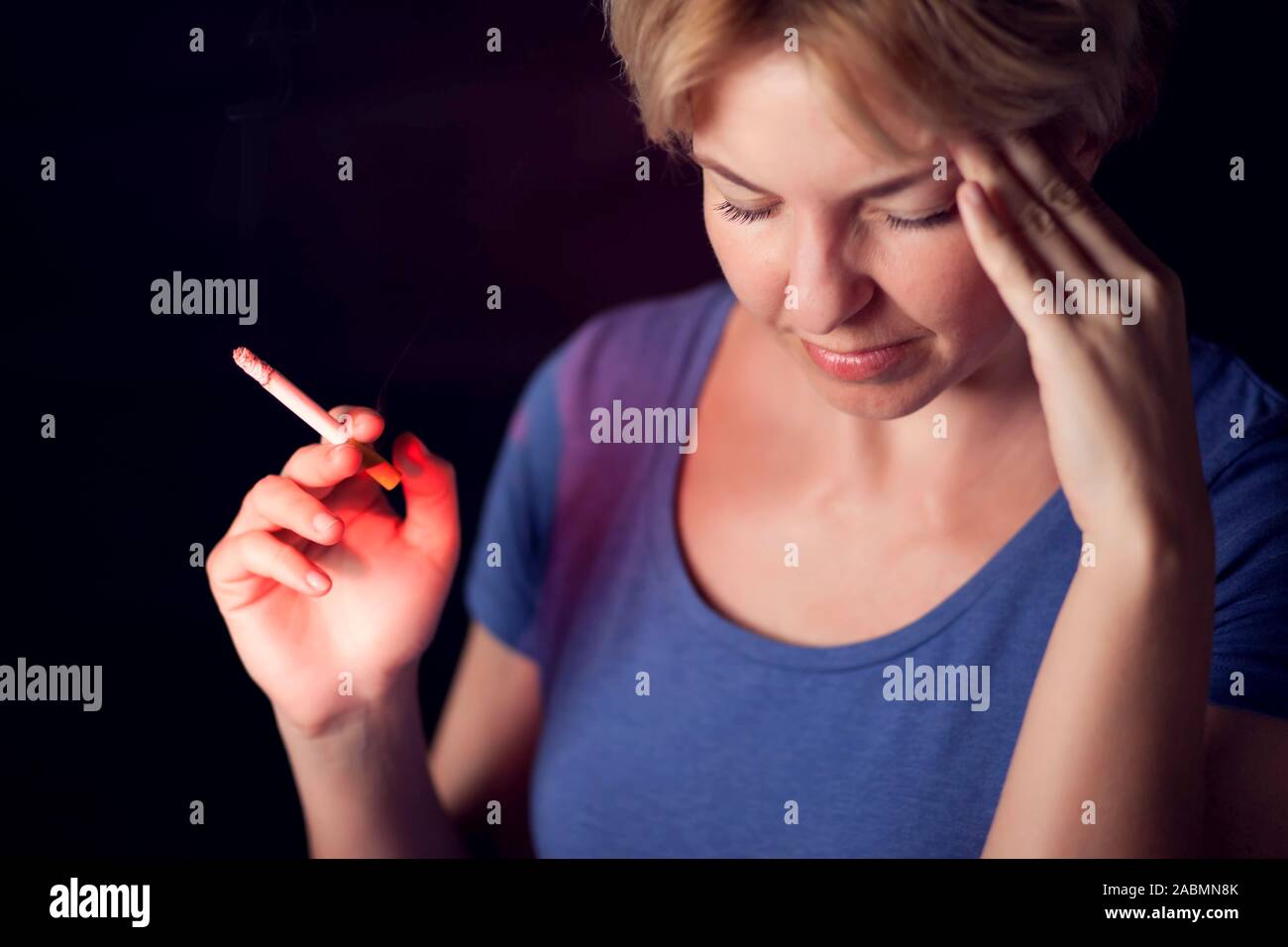 Mujer fuma cigarrillos y tiene fuertes dolores de cabeza. La adicción al tabaco y el problema de salud concepto Foto de stock
